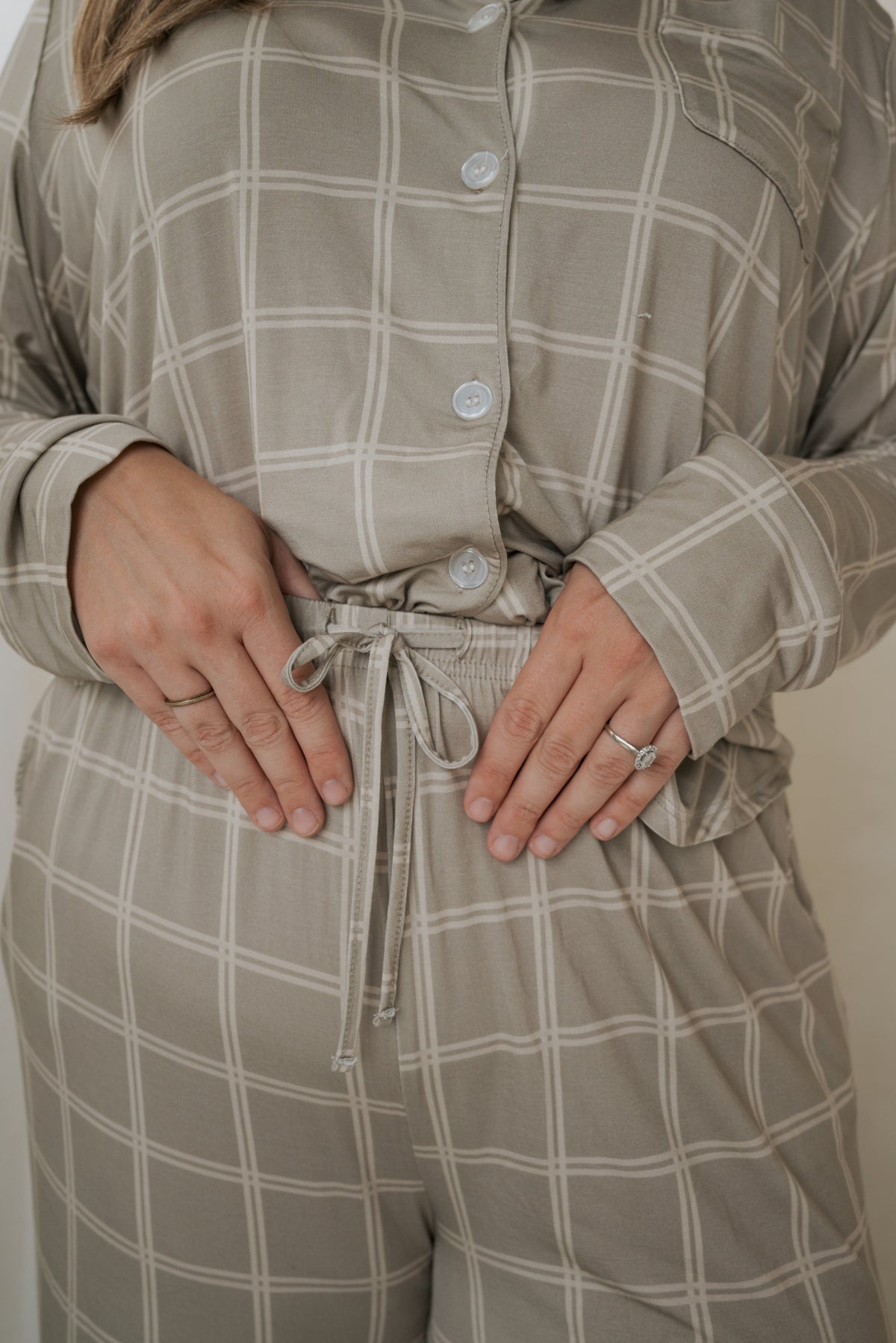 A person wearing a Women’s Bamboo Button Up Lounge Set | Linen Grid in a tan and white pattern, featuring a button-up top and wide leg lounge pants with a drawstring waistband.