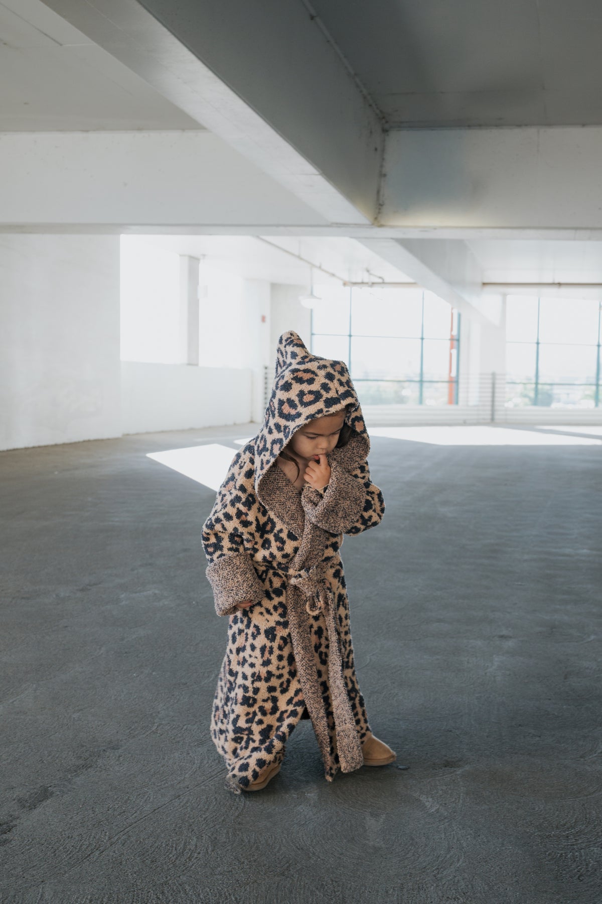 A toddler wearing a hooded Children’s Robe | Leopard made of microfiber feather yarn standing in a parking garage.