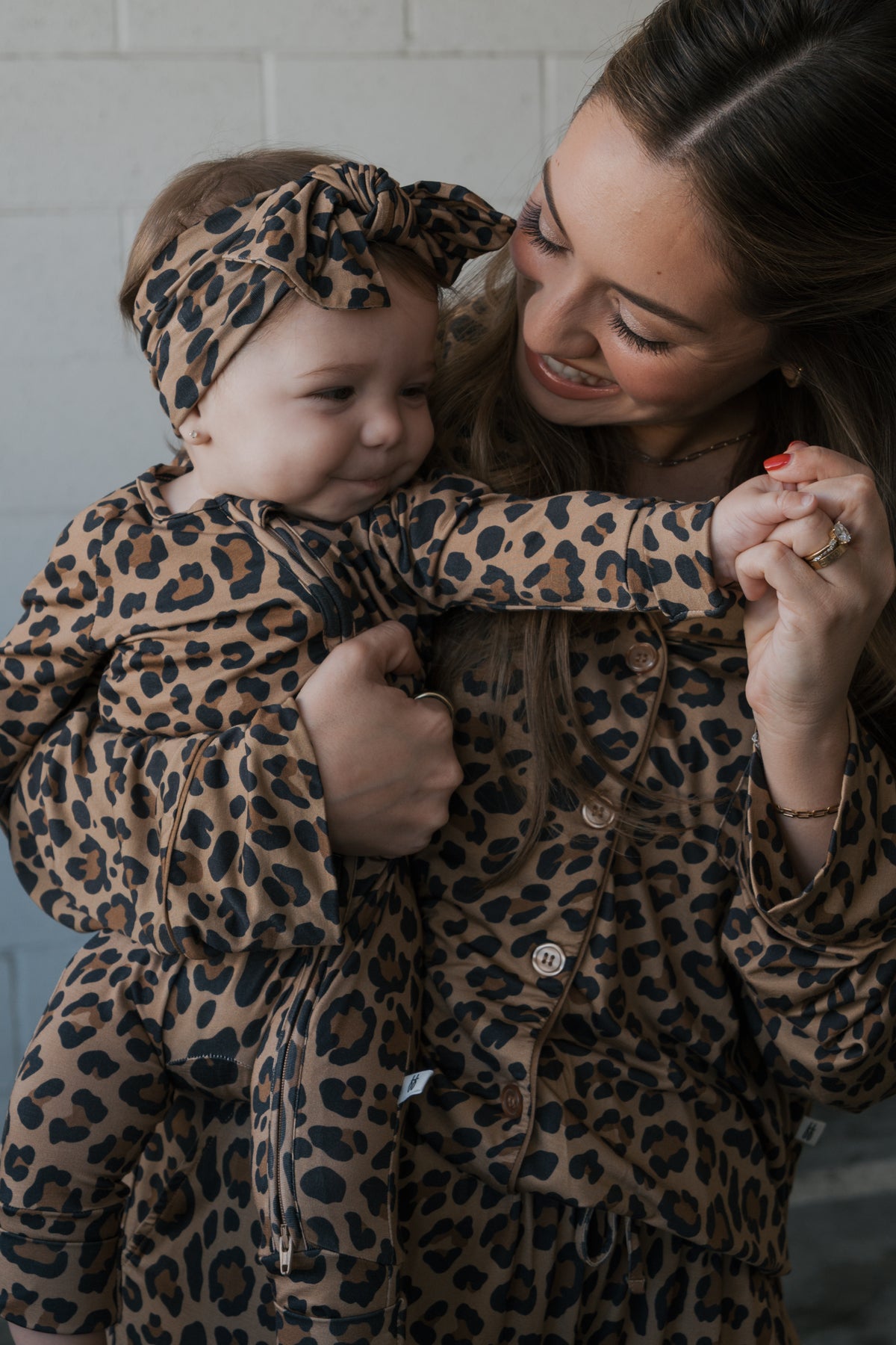 A mother holding her baby in matching leopard print outfits, with the baby wearing Bamboo Zip Pajamas | Leopard and a matching headband.