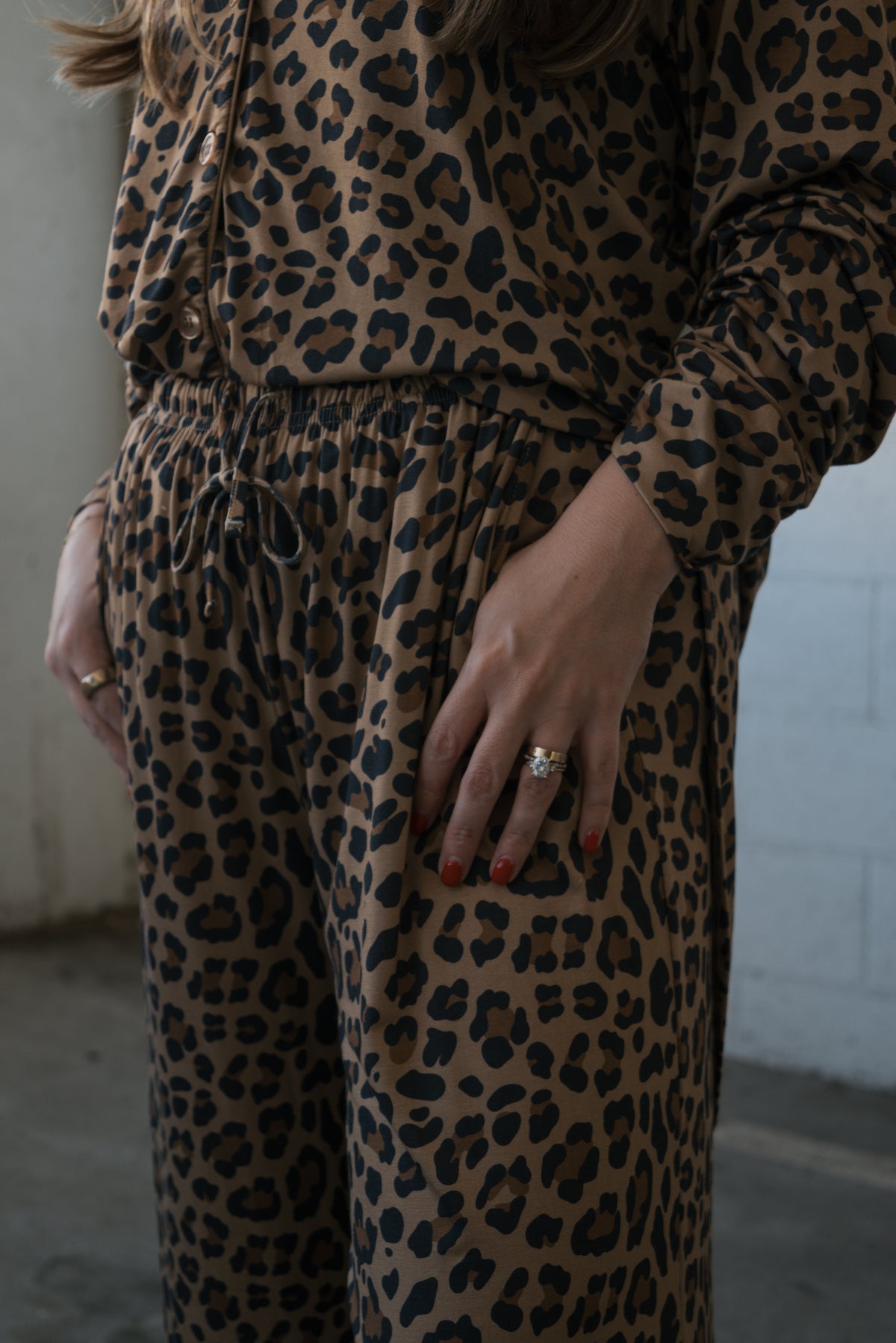 A person wearing a forever french baby Women’s Bamboo Button Up Lounge Set in a brown leopard print, featuring a long-sleeved, button-up shirt and drawstring pants.