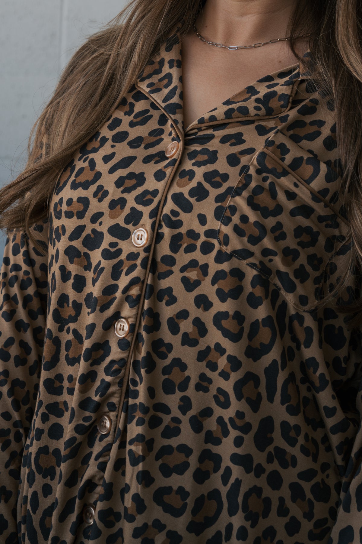 A woman wears the Women’s Bamboo Button Up Lounge Set | Leopard, featuring a long-sleeved, button-down lounge shirt in a brown and black leopard print.