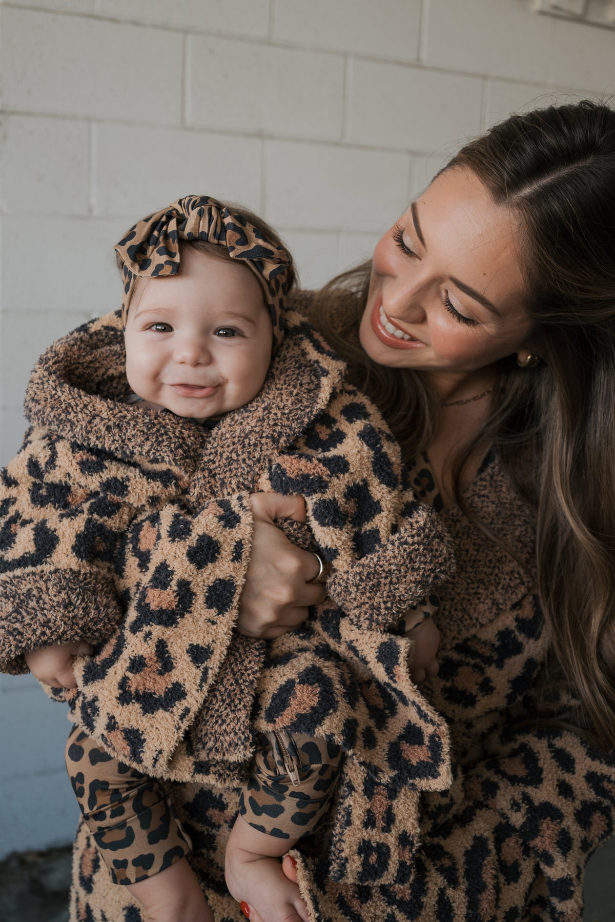 A woman holds a baby wearing an Oeko-tex certified Children’s Robe | Leopard with a matching head wrap.