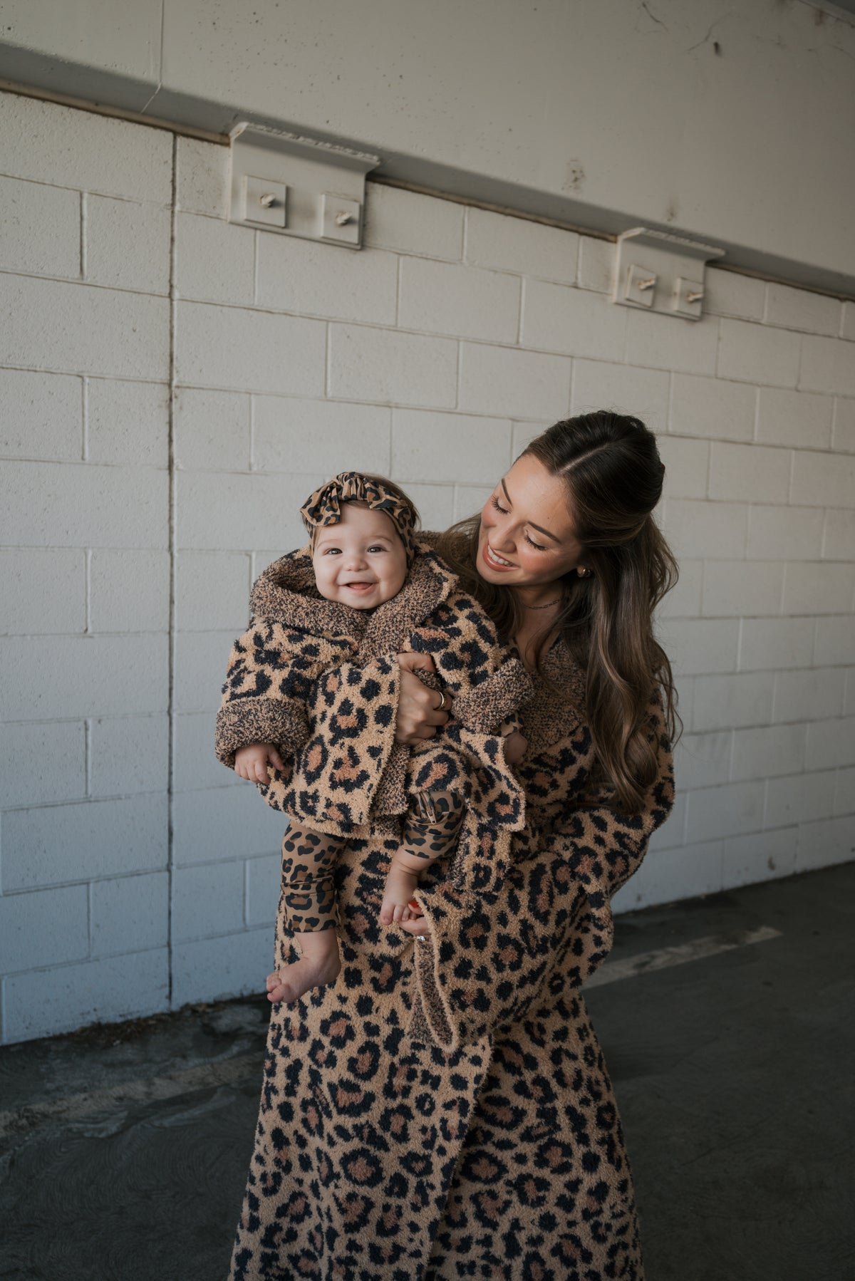 A woman smiling as she holds a baby, both wearing matching Adult Robe | Leopard by forever french baby.