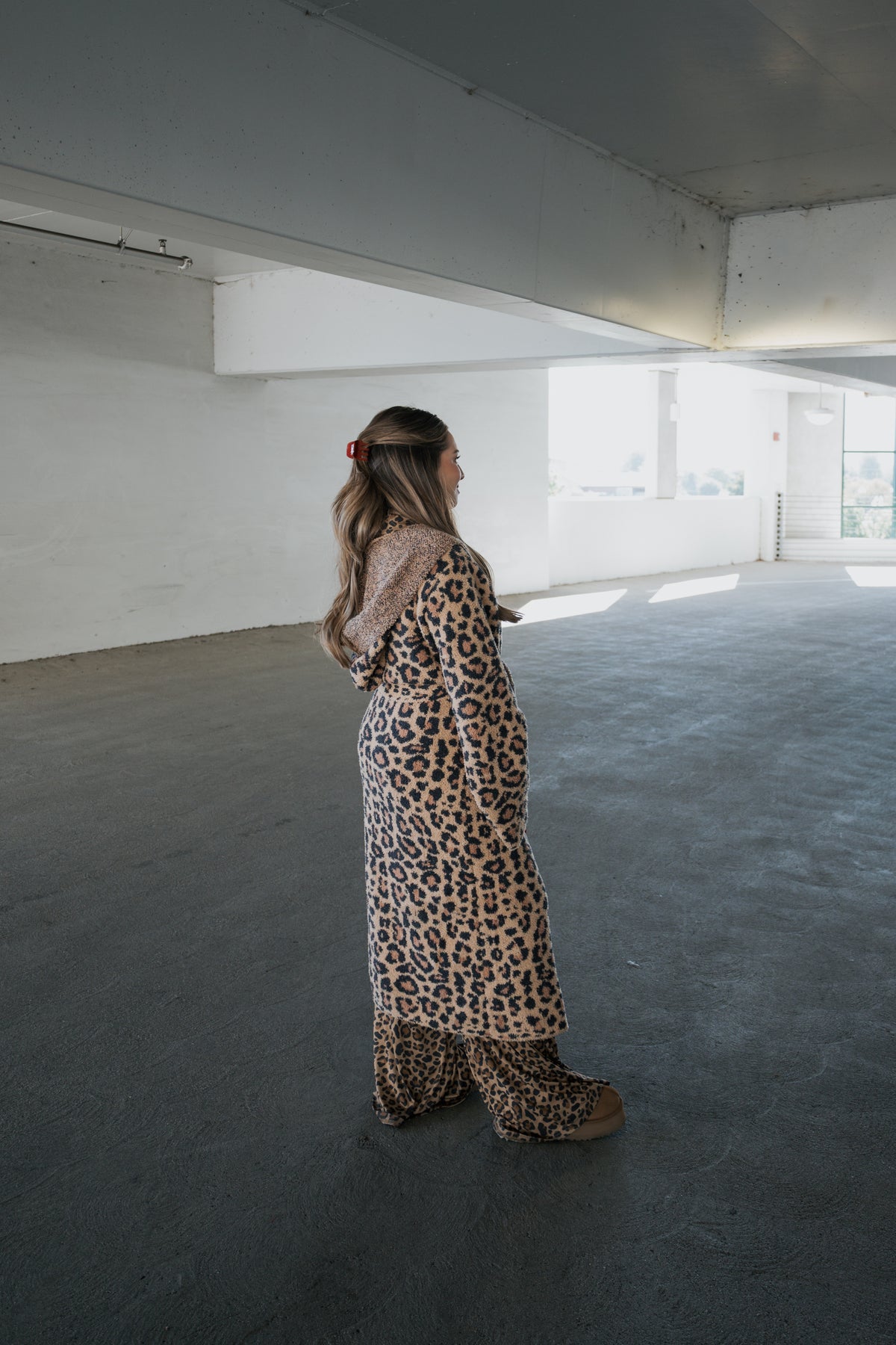 A woman stands in a parking garage wearing a full-length, leopard-print Adult Robe | Leopard in microfiber with matching wide-leg trousers.