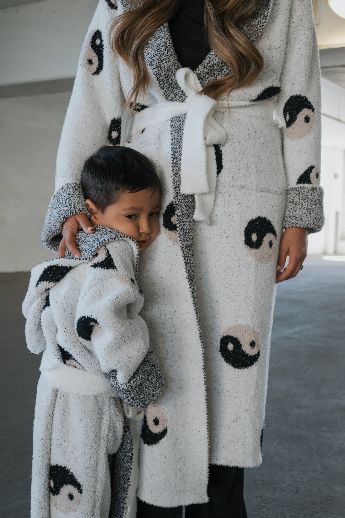 A young child wearing a fuzzy Children’s Robe | Yin Yang leans against an adult in a matching robe.