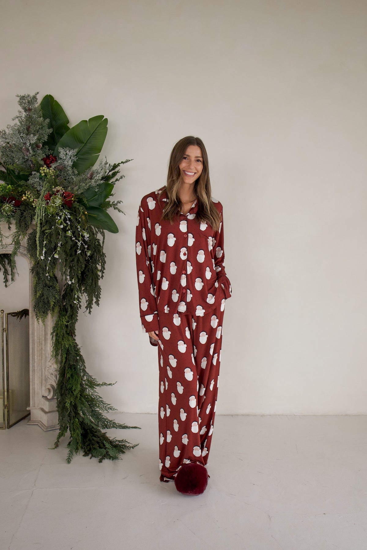A woman wearing the forever french baby Women’s Bamboo Button Up Lounge Set in Vintage Santa, featuring a button-up long-sleeve shirt and matching wide-leg lounge pants in a dark red fabric patterned with white Santa Claus figures.