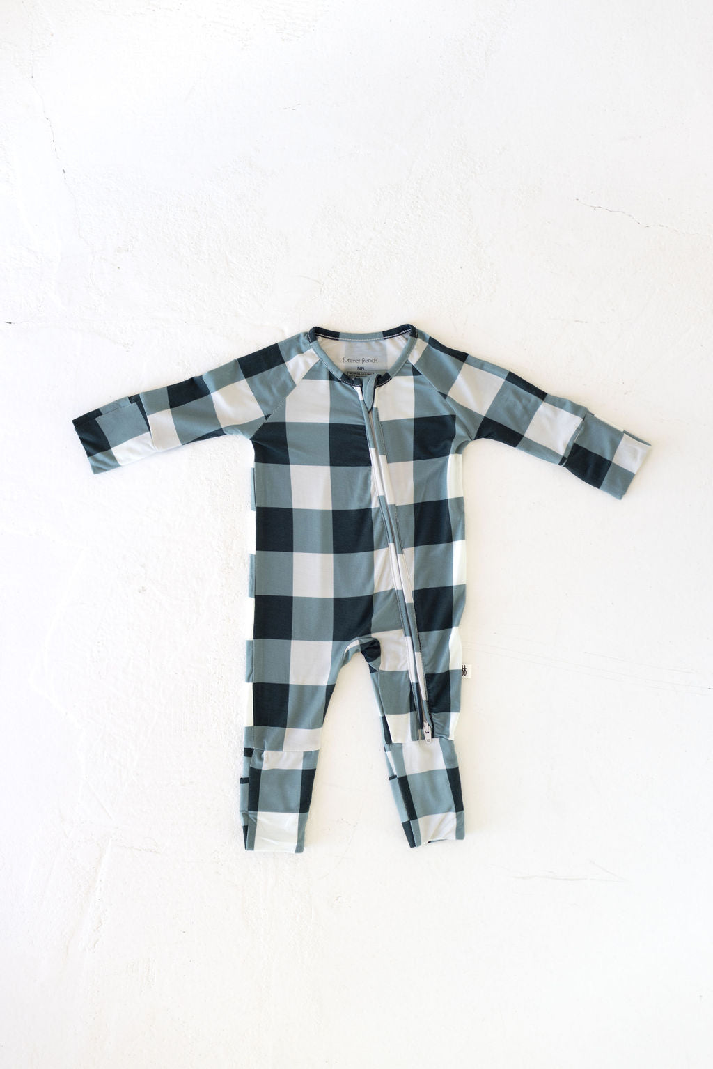 Introducing the Bamboo Zip Pajamas in Evergreen Gingham from forever french baby. This hypo-allergenic onesie features long sleeves and a convenient front zipper, crafted from breathable fabric with a charming checkered pattern of alternating dark green and light blue squares. Laid flat against a white background, these pajamas are designed to keep your little one's sensitive skin comfortable.