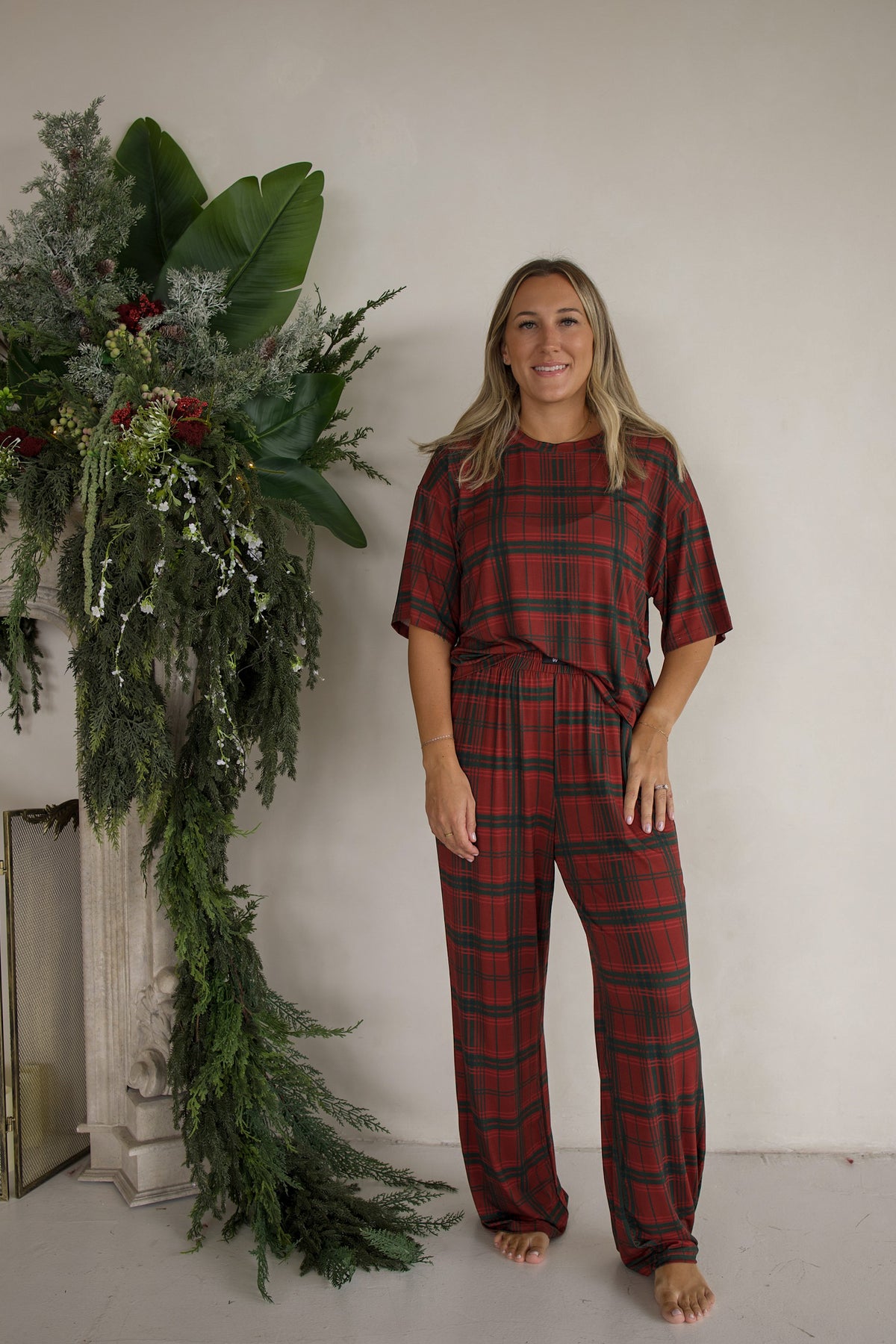 A woman wears a Women’s Boxy Tee Lounge Set in Christmas plaid, featuring a short-sleeved boxy t-shirt and loose-fitting hypo-allergenic pants.