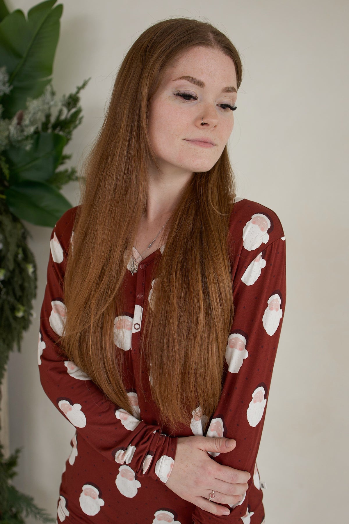 A woman wearing dark red, long-sleeve Women’s Long Sleeve Bamboo Pajama | Vintage Santa featuring a repeating pattern of Santa Claus faces.