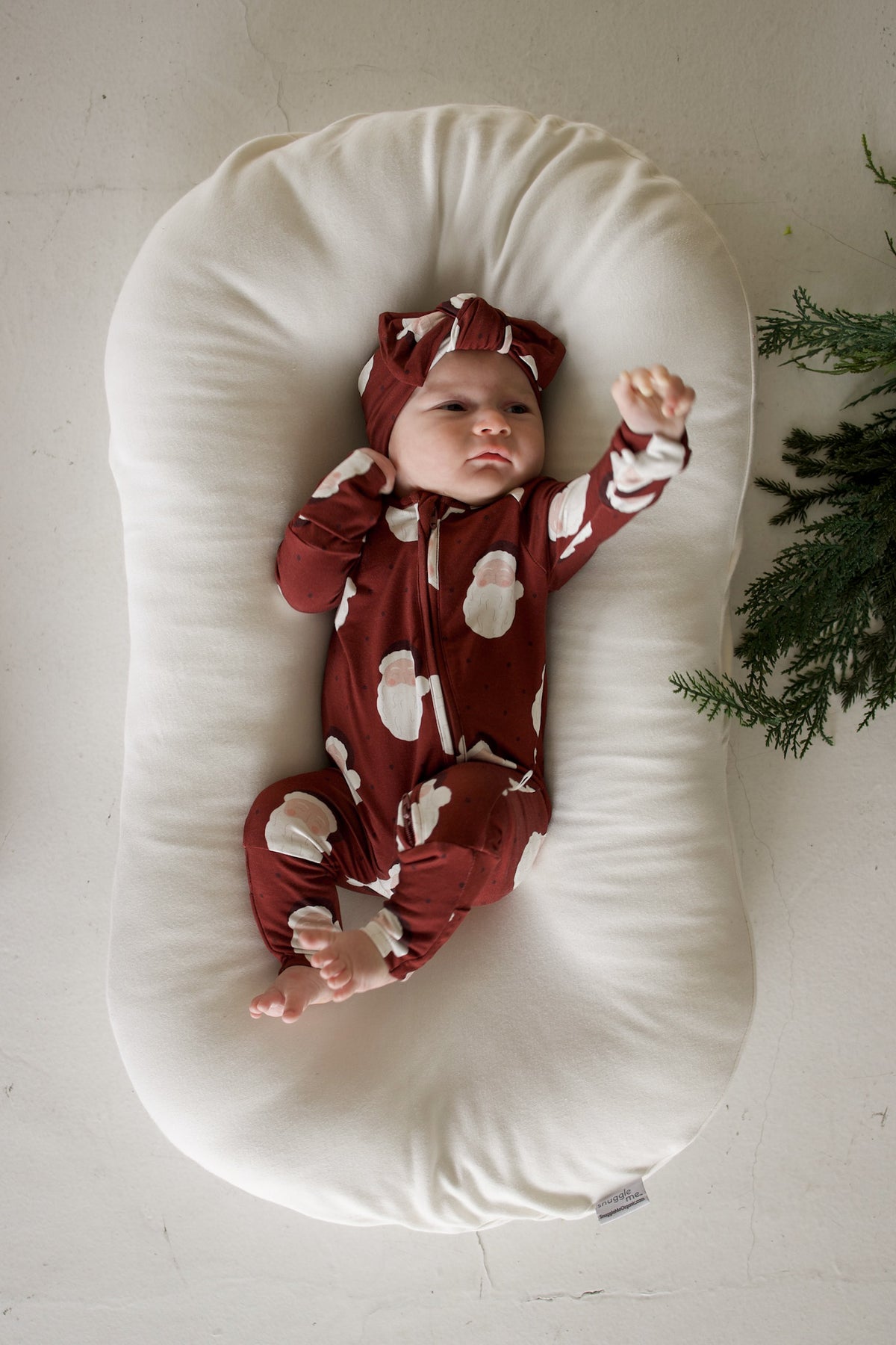 A baby wears Bamboo Zip Pajamas | Vintage Santa with a matching headband while lying in a white lounger.
