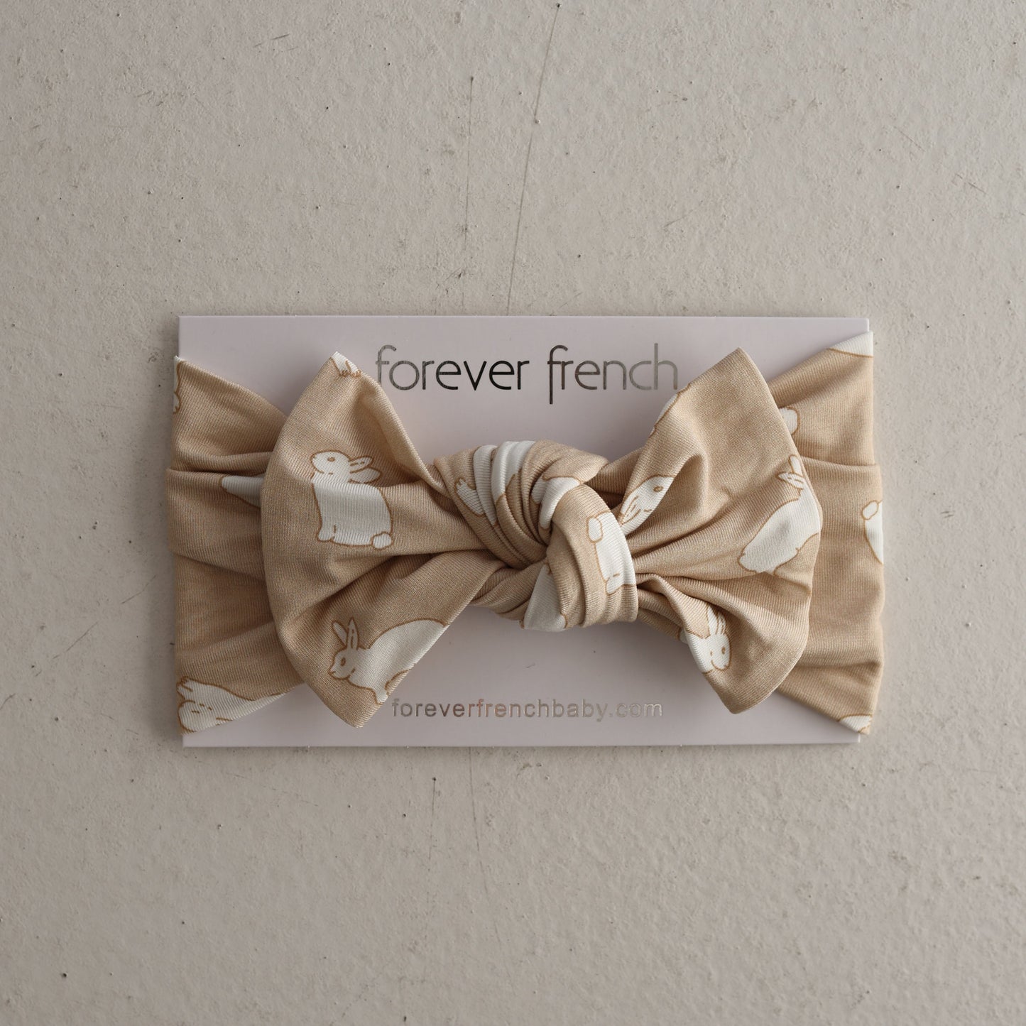 The Bamboo Head Wrap | Bunnies by forever french baby is a beige knotted baby bow headband featuring white bunny prints, shown on a “forever french baby” card against a neutral backdrop.