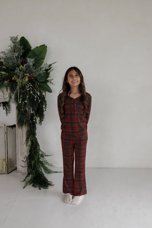 A girl wearing the Youth Flare Bamboo Pajamas | Christmas Plaid by forever french baby, featuring long sleeves and flared bottoms in red and green plaid.
