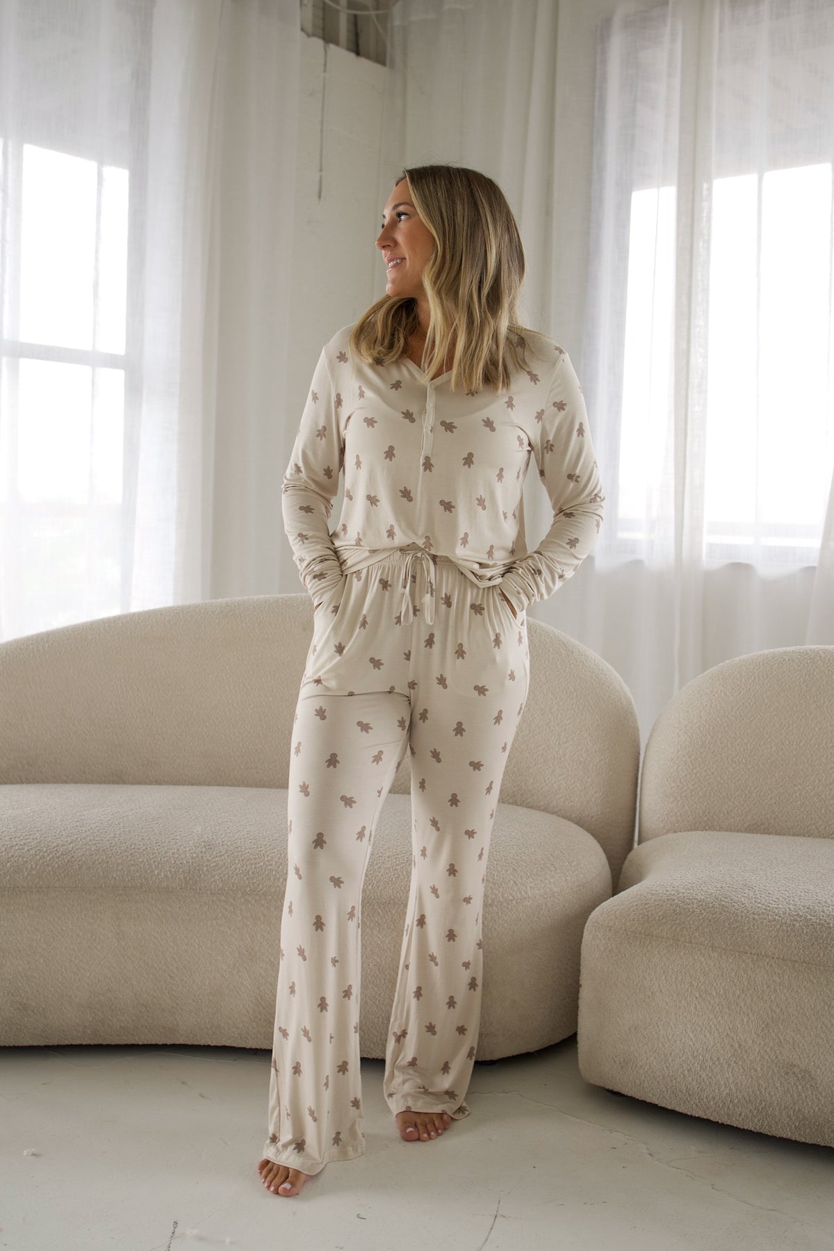 A woman wears a Women’s Long Sleeve Bamboo Pajama | Gingersnap set, featuring a long-sleeve top and bottoms with a gingerbread man print.