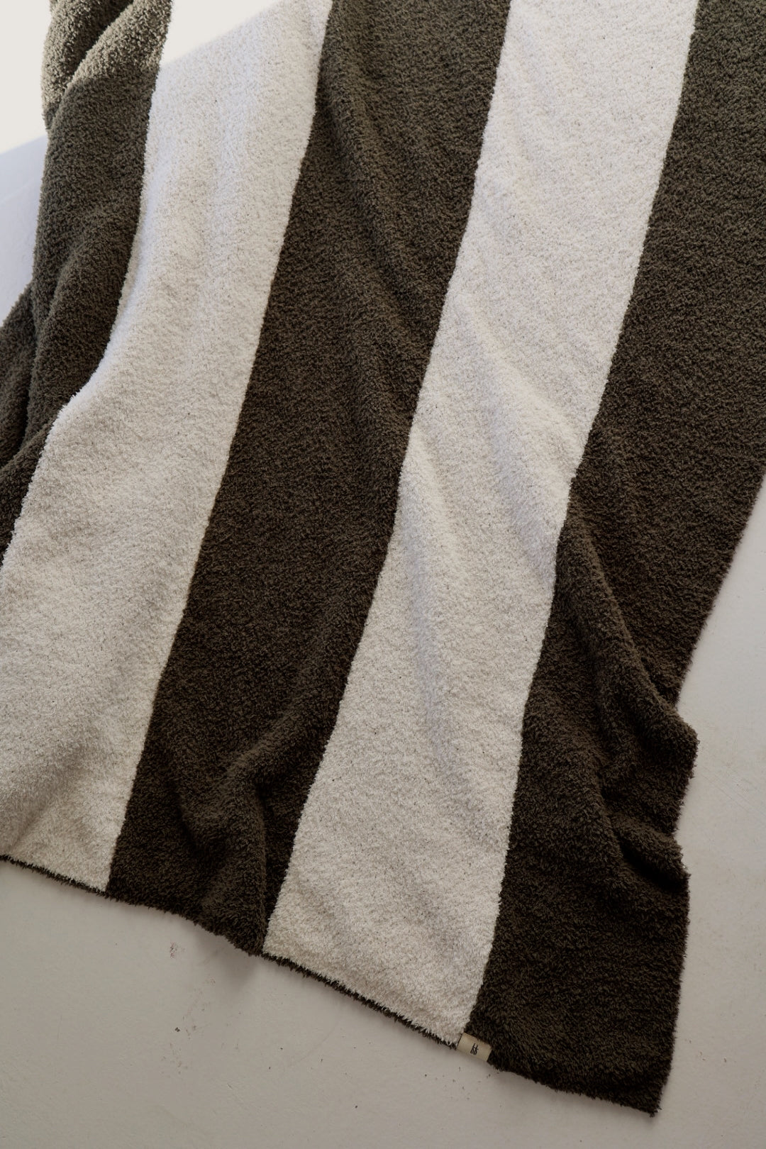 The forever french baby Plush Blanket | Fireside Stripe features wide dark gray and white stripes, offering velvety softness and cozy style to any space. Draped over a light surface, it adds warmth and charm.