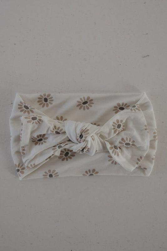 The forever french baby Bamboo Head Wrap | Daisy Fields is shown laid flat on a light surface, featuring brown daisy prints on white bamboo fabric with a decorative central knot.