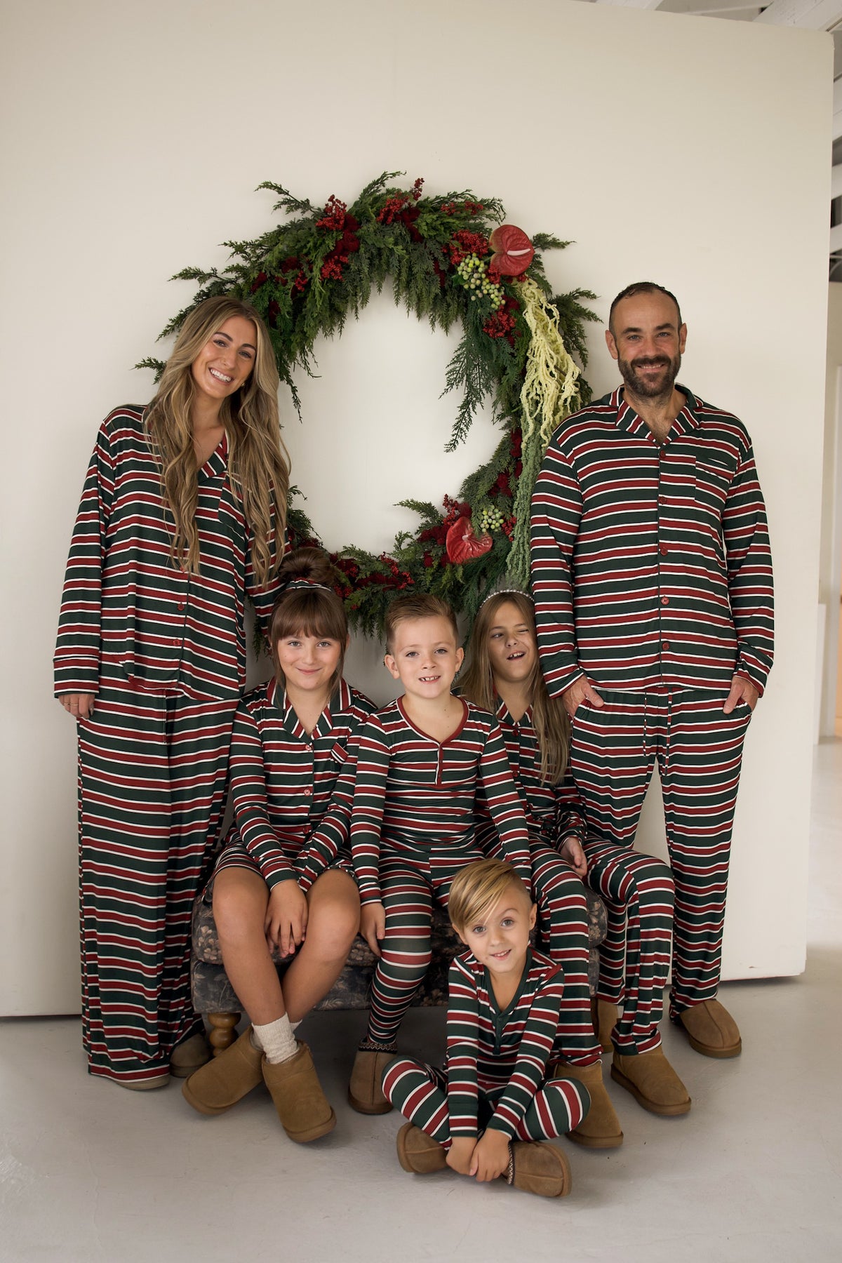 A family of six wearing matching green, red, and white striped Men’s Bamboo Button Up Lounge Set | Holiday Stripe pajamas, posing in front of a holiday wreath.
