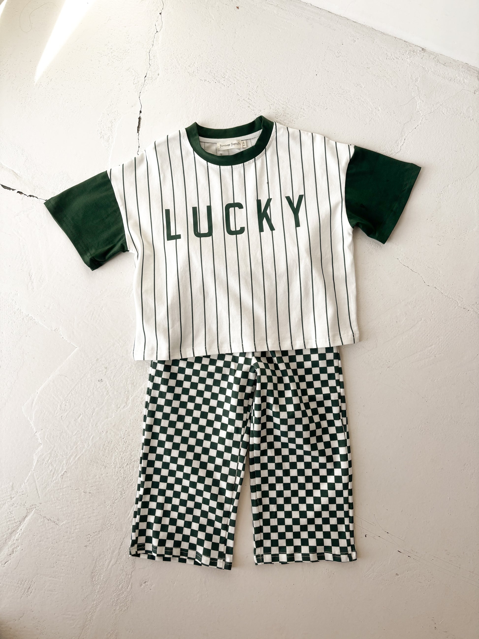 The forever french baby T-Shirt & Pant Set | Lucky Micro Check features a white short-sleeve shirt with green sleeves, black stripes, "LUCKY" on the front, and green checkerboard shorts for a playful children's daywear look.