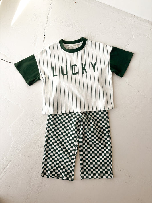 The forever french baby T-Shirt & Pant Set | Lucky Micro Check features a white short-sleeve shirt with green sleeves, black stripes, "LUCKY" on the front, and green checkerboard shorts for a playful children's daywear look.