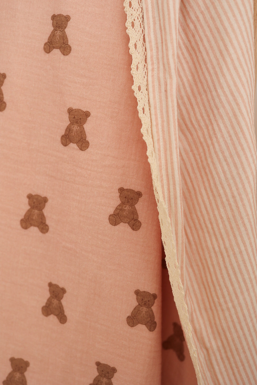 A close-up of forever french baby’s Muslin Quilt | Pink Lottie & Sadie Stripe shows pink teddy bear print and beige-white stripes, divided by cream lace—ideal for nursery bedding or a cozy baby quilt.