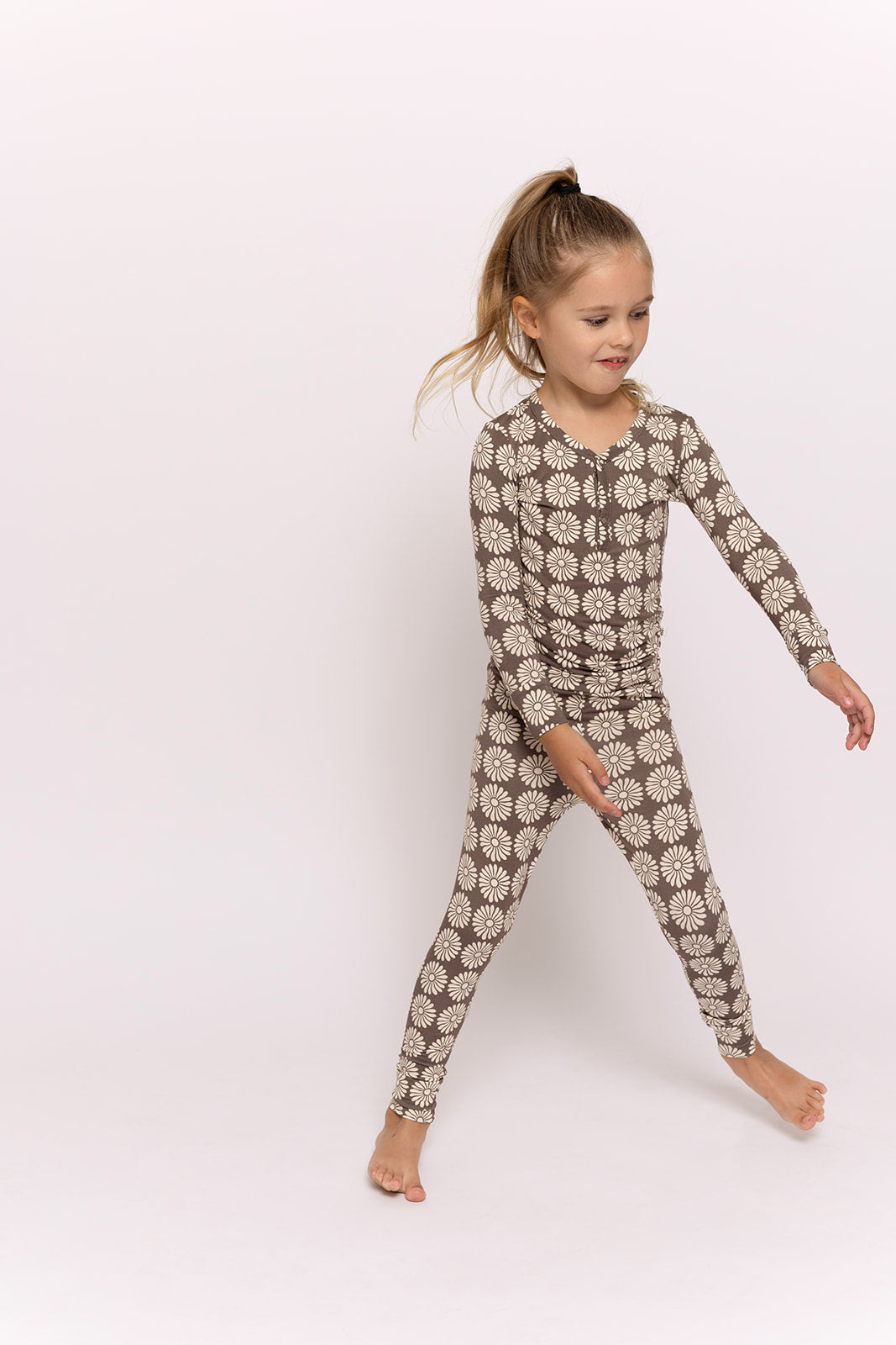 A young girl with a ponytail wears forever french baby’s Bamboo Two Piece Pajamas in Retro Floral, featuring long sleeves and a playful daisy print—breathable sleepwear perfect for sweet dreams.