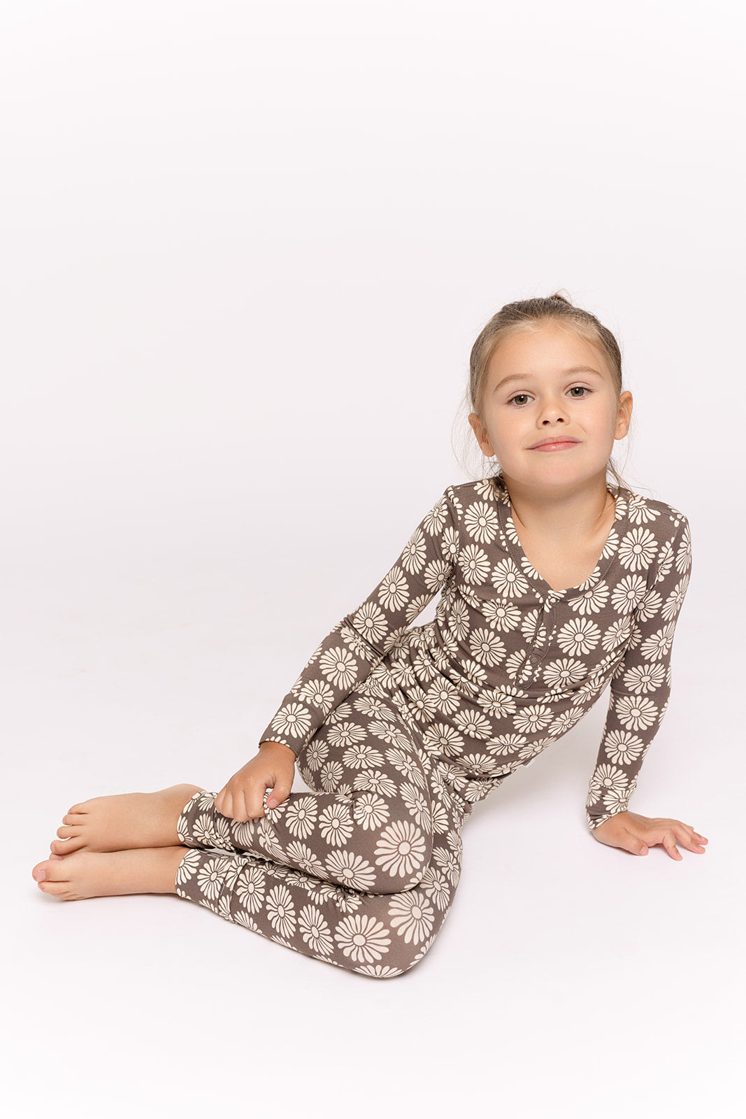 A young girl sits on the floor against a white background, wearing forever french baby’s Bamboo Two Piece Pajamas in Retro Floral. She looks at the camera with a relaxed expression—perfect cozy sleepwear for kids.
