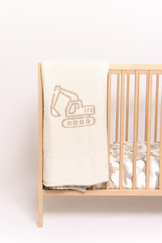 The Plush Blanket | Excavator by forever french baby is a cozy cream microfiber blanket with an excavator outline, draped over a light wood crib. OEKO Standard 100 certified for safety.