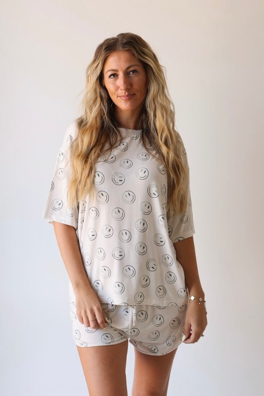A woman with long wavy hair models the forever french baby Women's Bamboo Short Set in Green Smiles—featuring hypo-allergenic bamboo viscose and smiley face prints—against a plain light background.