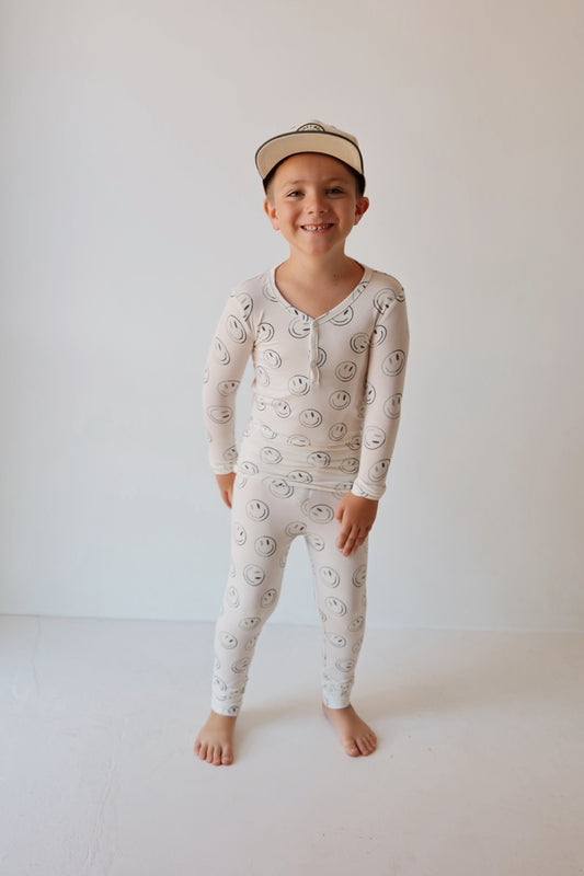 A smiling young boy stands barefoot against a white background, wearing forever french baby’s Bamboo Two Piece Pajamas in Green Smiles—soft, breathable sleepwear for all-night comfort.