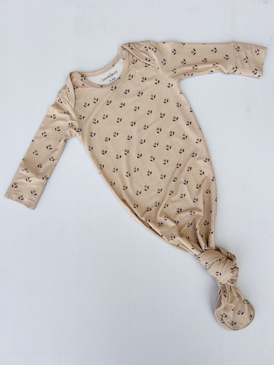 The "Bamboo Knotted Gown | Flora" by forever french baby is a beige, hypo-allergenic bamboo gown with long sleeves and a knotted bottom. It features a subtle black arrow pattern against a white background, making it an essential for newborns.