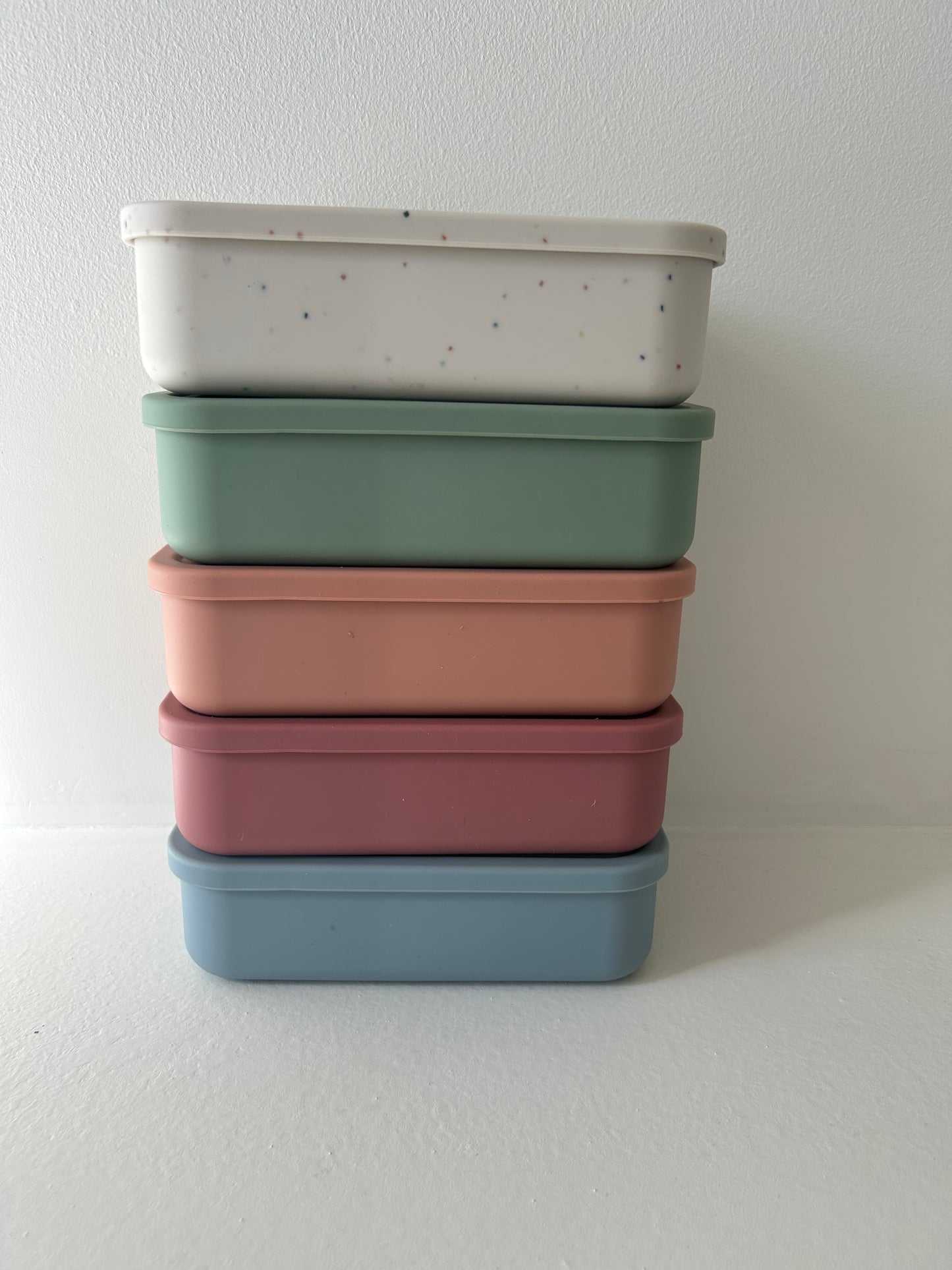 A set of four pastel-colored, BPA-free silicone Bento Boxes by forever french baby (speckled white, green, peach, and blue) is neatly aligned against a plain white background. These colorful storage containers provide both style and durability for your lunch needs.