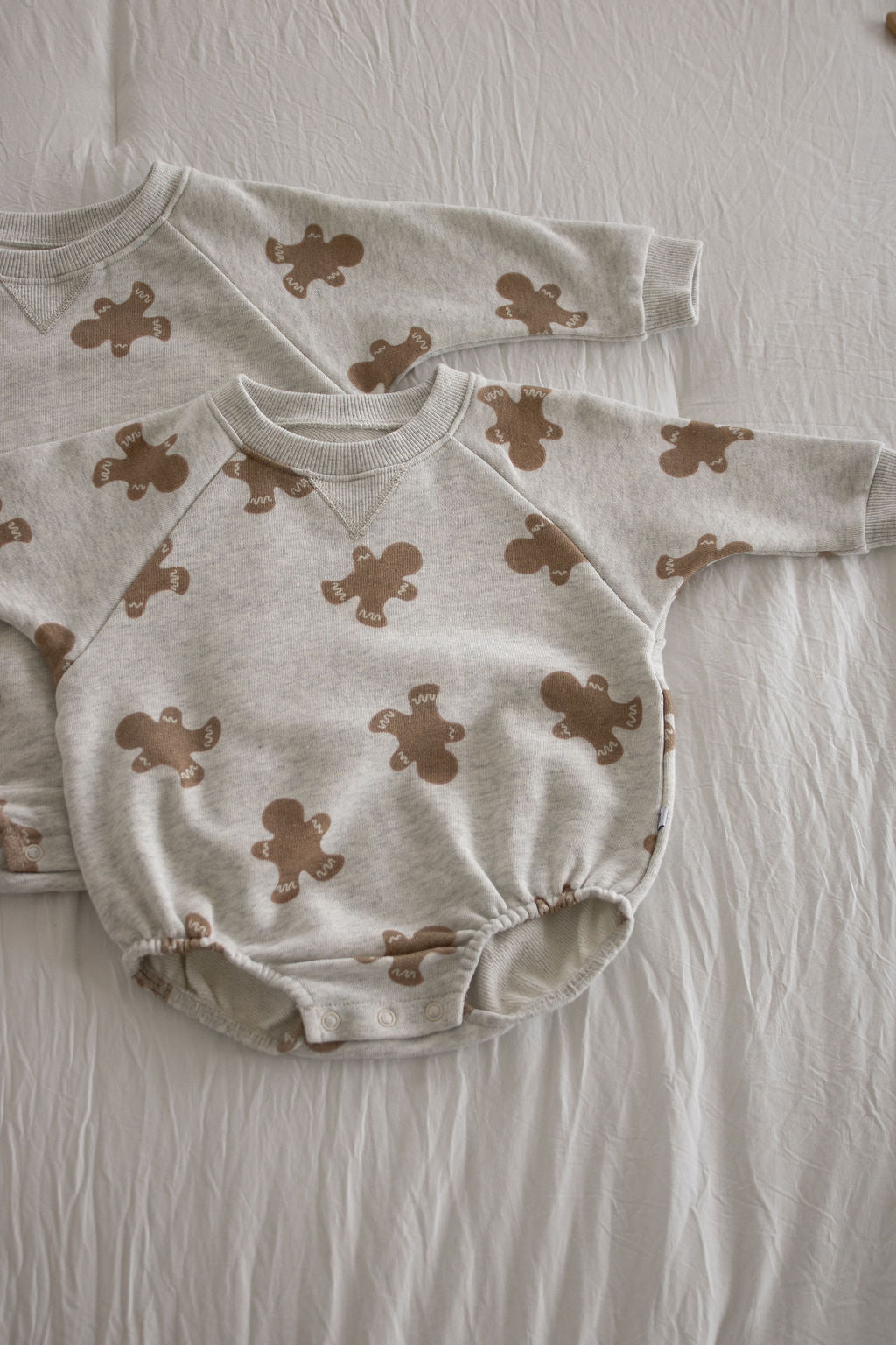 Two forever french baby Sweatshirt Romper | Gingerbread 2.0 in light gray with brown gingerbread patterns are laid flat, one slightly overlapping the other—ideal for comfy and stylish newborn wear.
