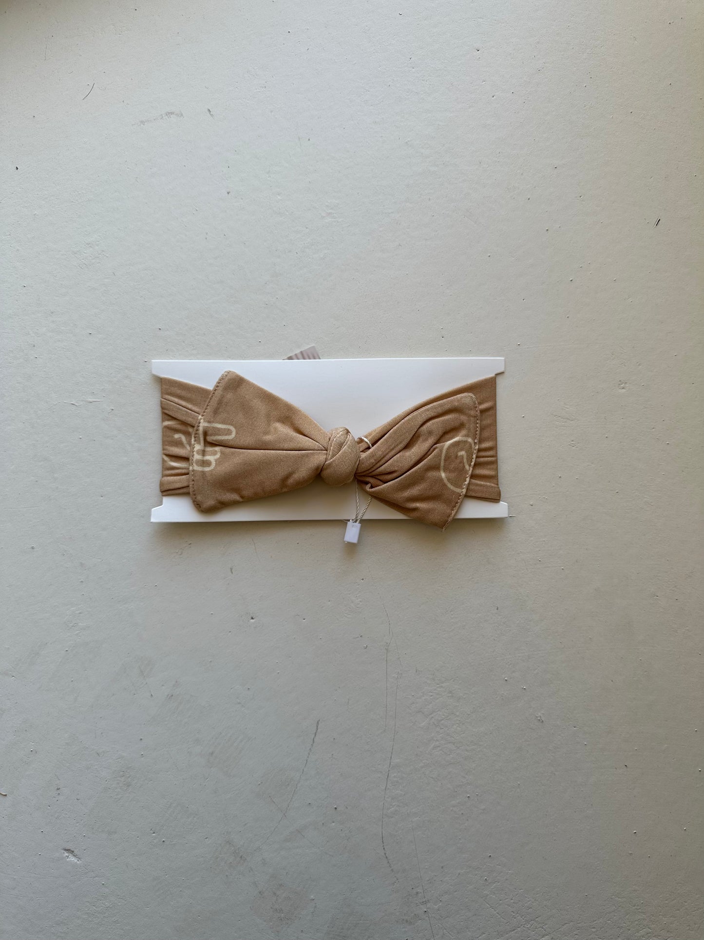 A "Bamboo Head Wrap | Peace Sign" by forever french baby, featuring a beige knotted bow design, is displayed on a white rectangular card against a light gray background.