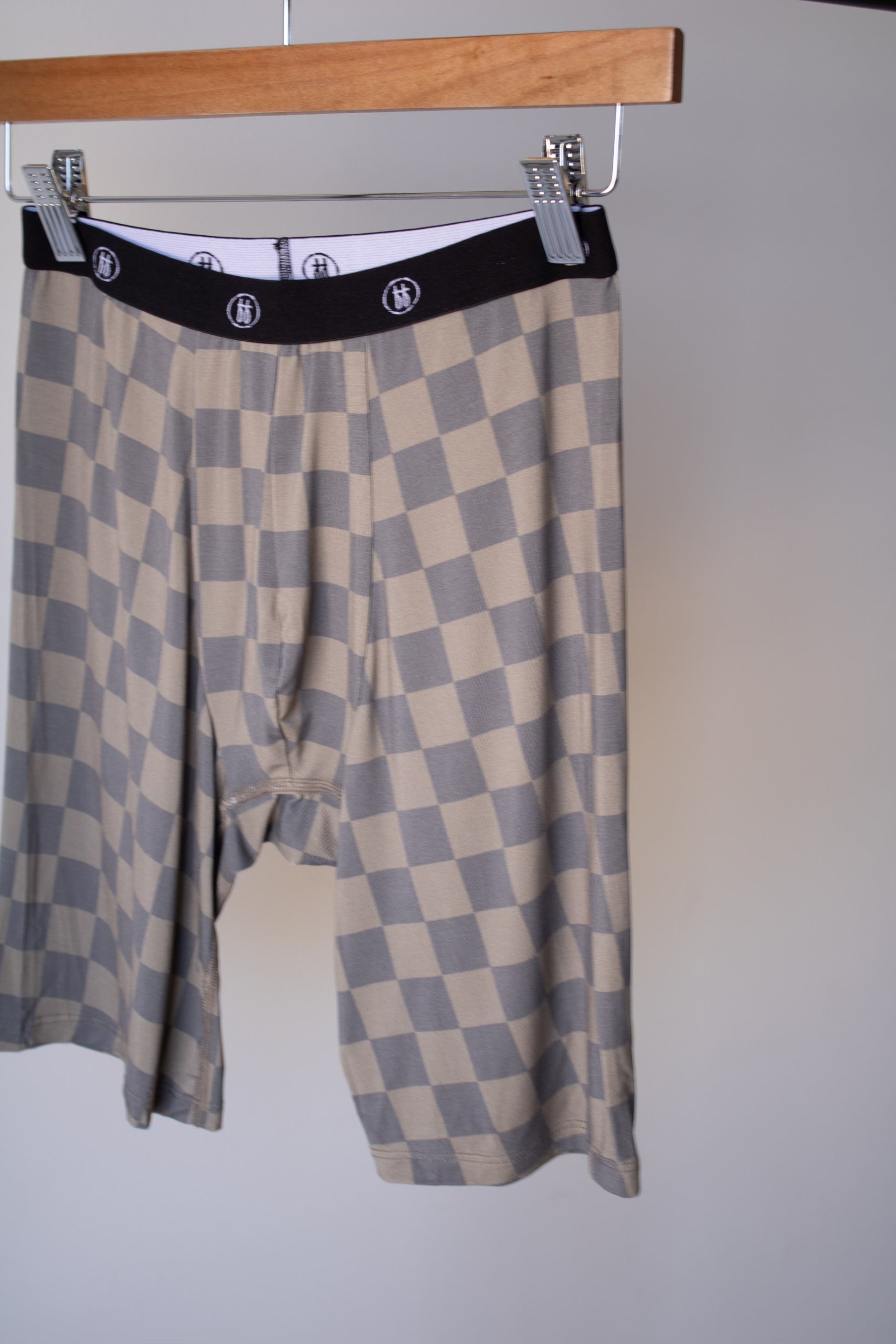 Forever french baby Men's Bamboo Boxers (3 Pack) in checkerboard and faded brown patterns, loose-fitting, knee-length with a black elastic waistband and white logo, shown hanging on a wooden hanger against a plain background.