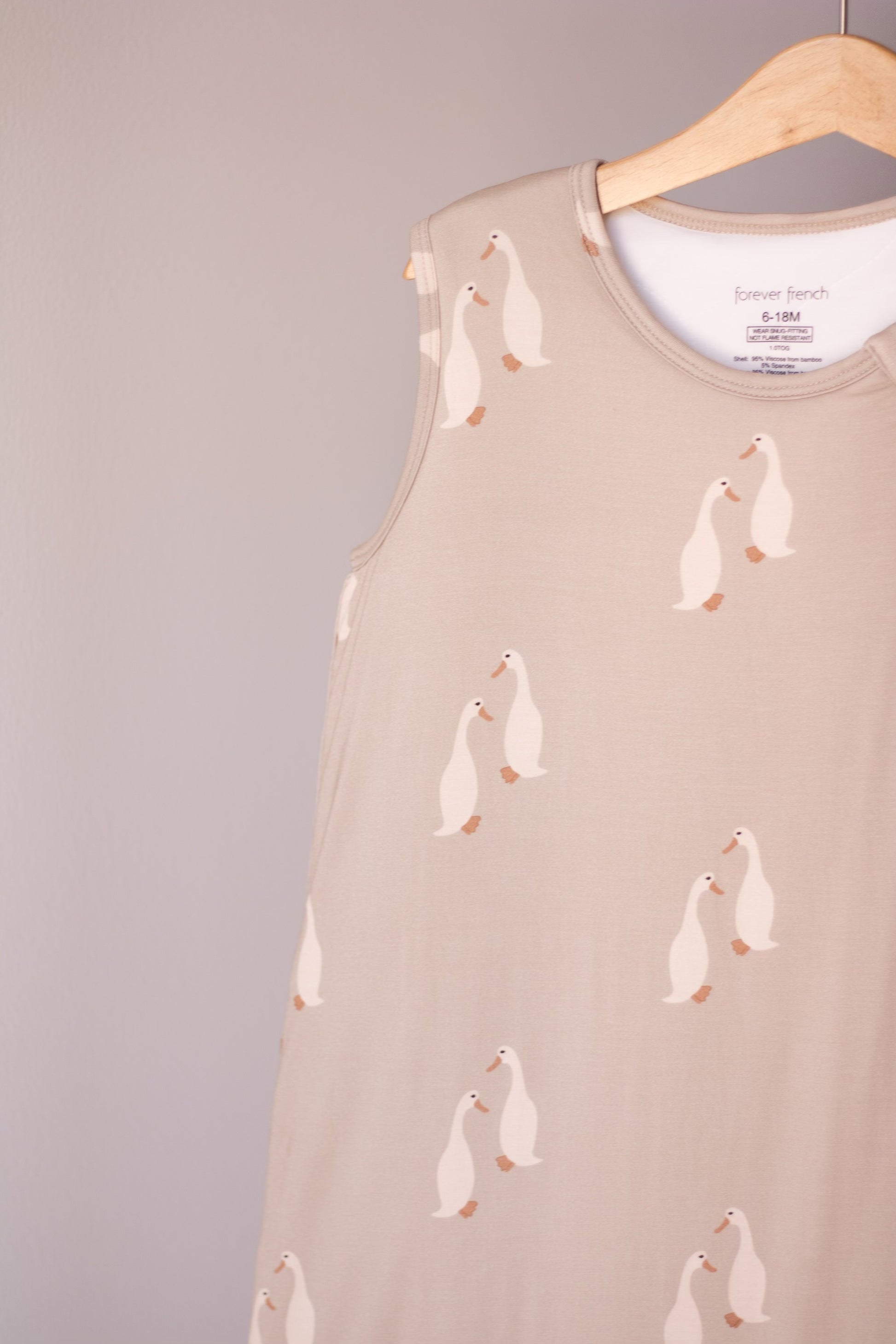 The Bamboo Sleep Sack | Silly Goose by forever french baby features a beige bamboo fabric with white geese, shown hanging on a wooden hanger against a light gray background. This cozy wearable blanket keeps your baby comfortable all night.
