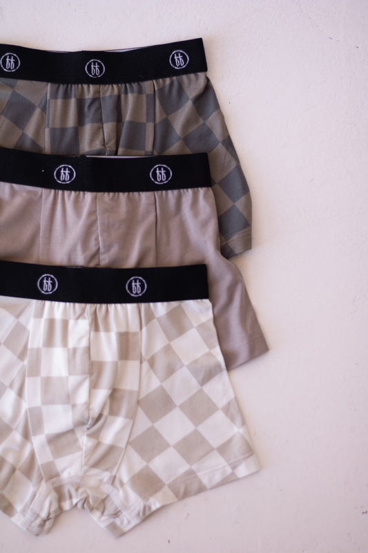 The Bamboo Boxers (3 Pack) by forever french baby features checkerboard and faded brown patterns with black waistbands—soft, hypo-allergenic underwear laid flat on a light surface for stylish comfort.