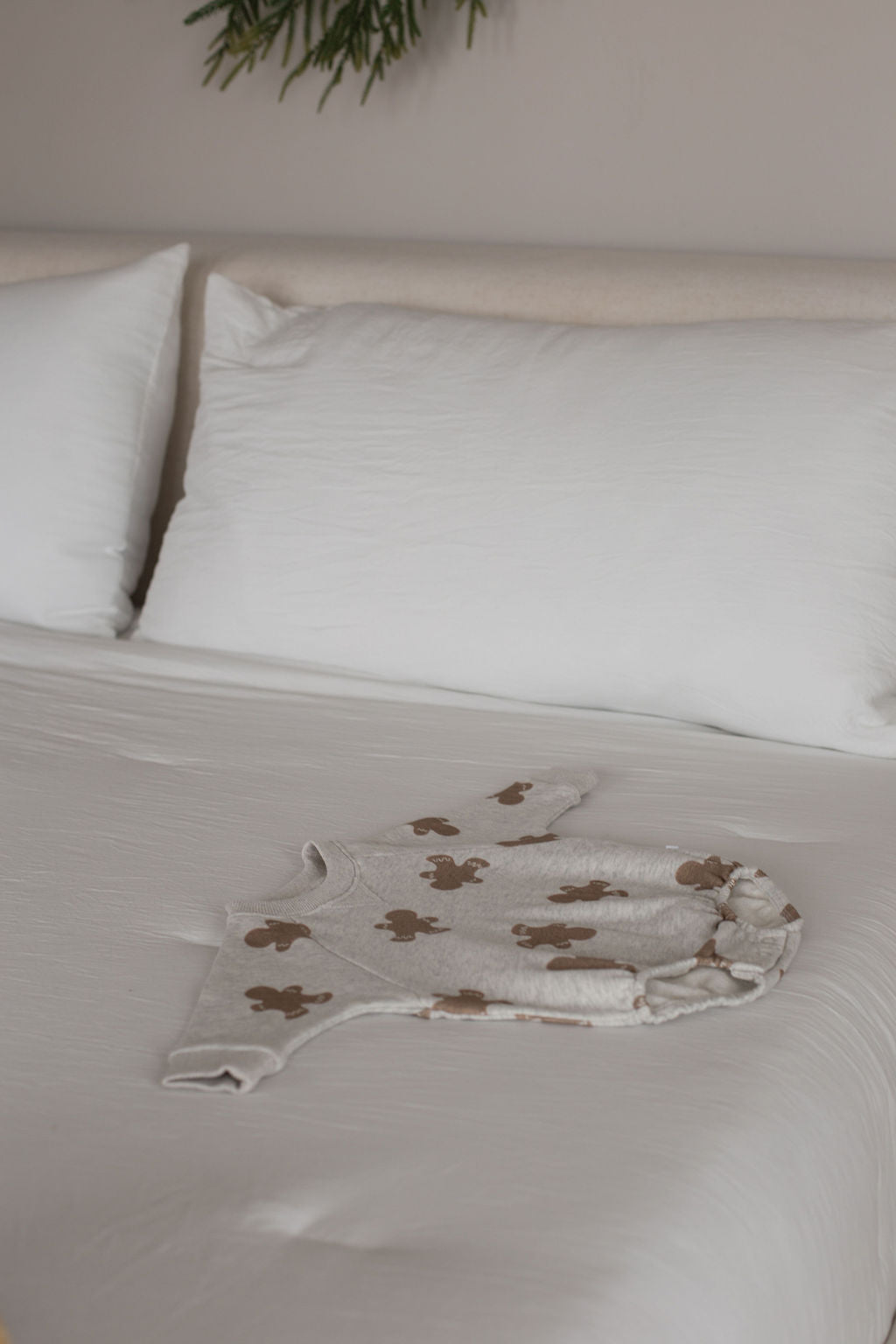 The forever french baby Sweatshirt Romper | Gingerbread 2.0, featuring a brown teddy bear pattern, is displayed on a neatly made bed with white sheets and pillows.