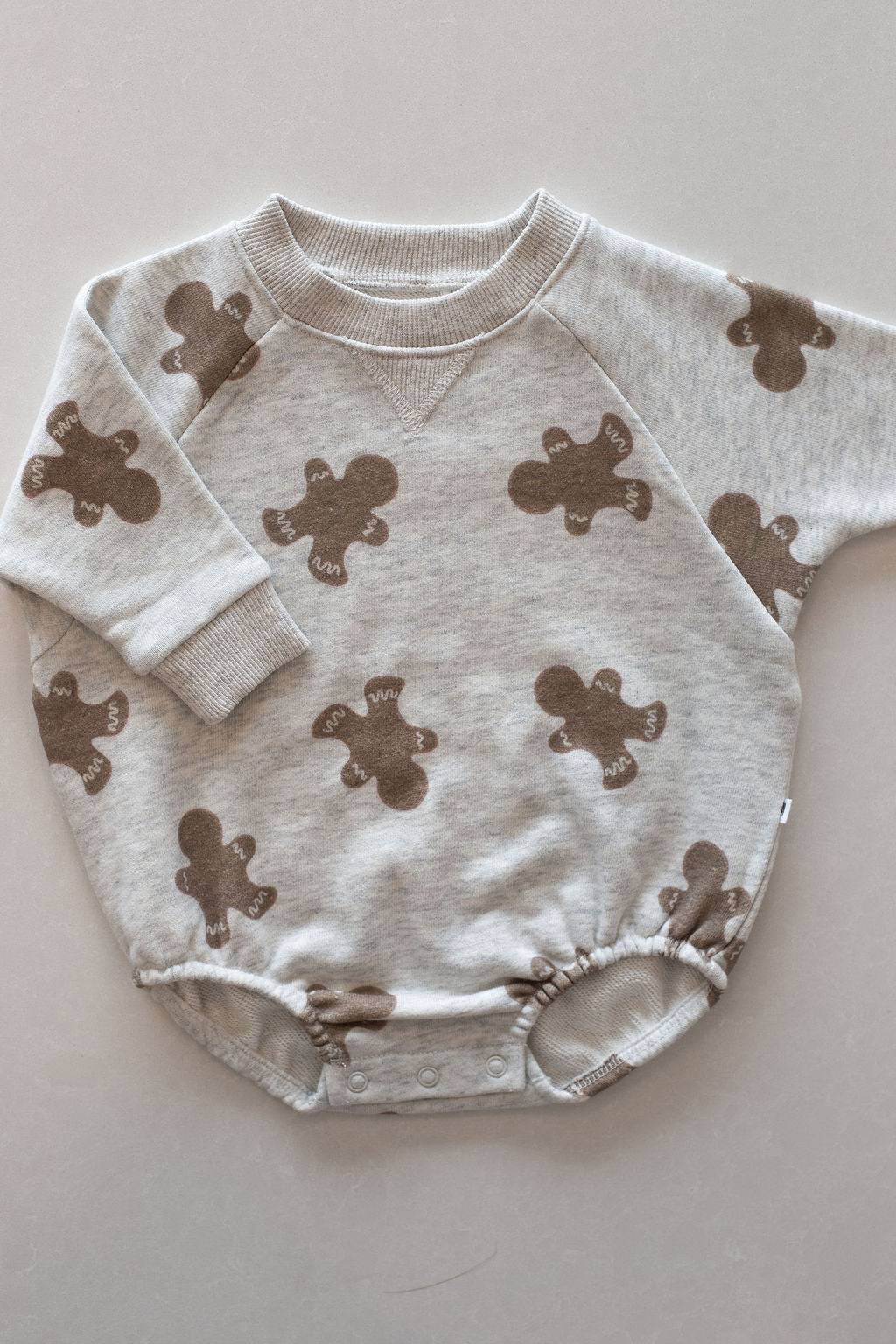 The forever french baby Sweatshirt Romper | Gingerbread 2.0 is a gray long-sleeve romper with gingerbread prints, ribbed cuffs, and snap buttons at the bottom—perfect cozy newborn clothing for easy diaper changes.