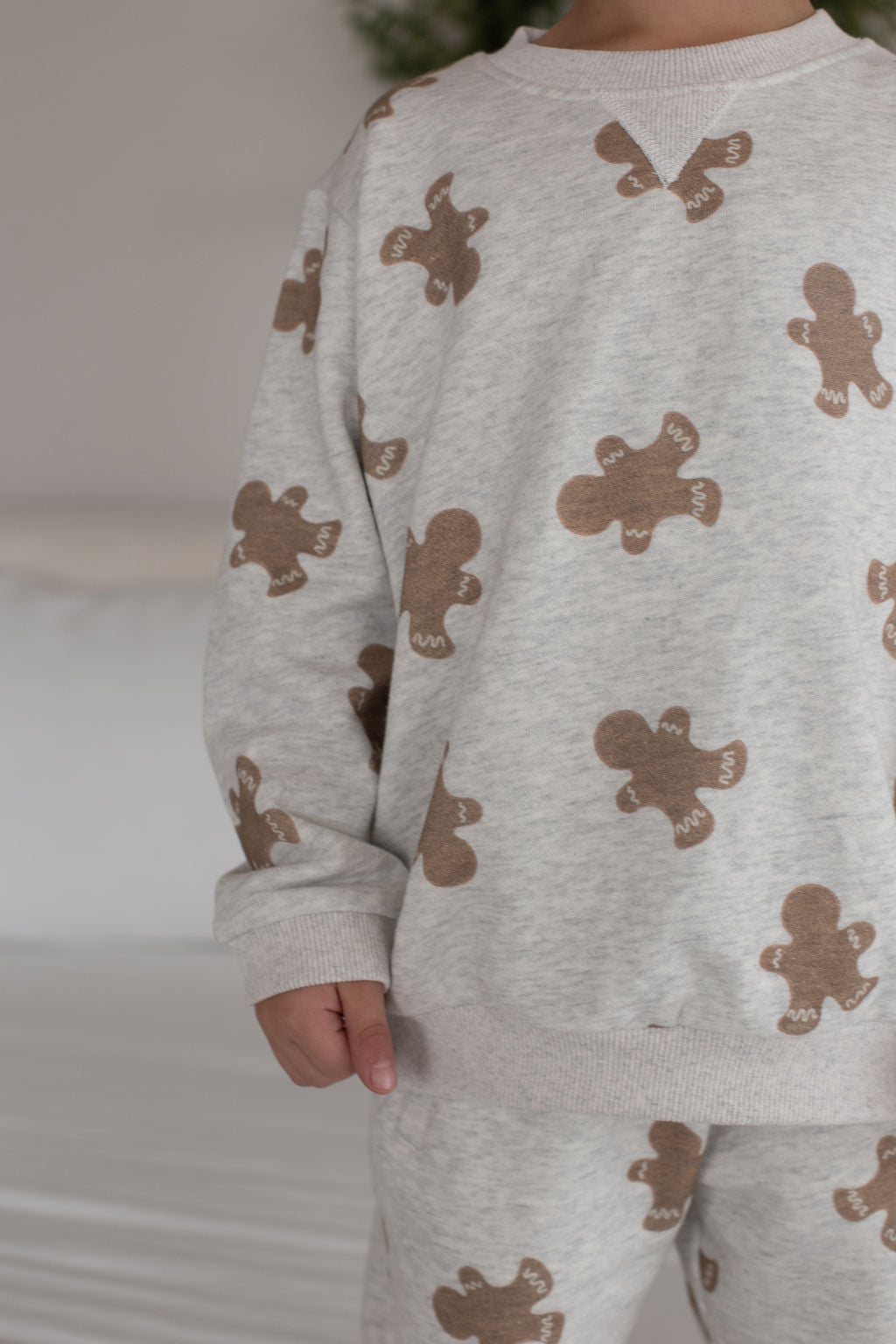 A child models the forever french baby Sweat Set | Gingerbread 2.0, a cozy outfit with a playful gingerbread print. The cropped photo shows only the child's lower face and body, highlighting stylish everyday moments.