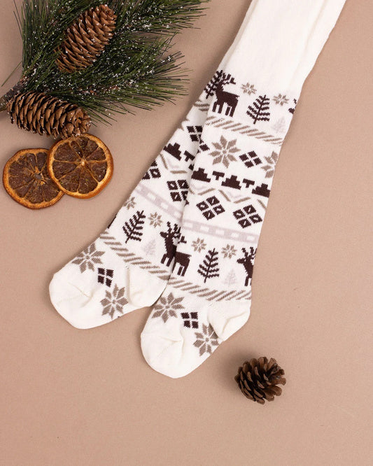 Little Millers Fair Isle Tight featuring brown and grey reindeer and snowflake motifs is displayed on a beige surface with pine branches, pine cones, and dried orange slices for a cozy, winter-inspired look.