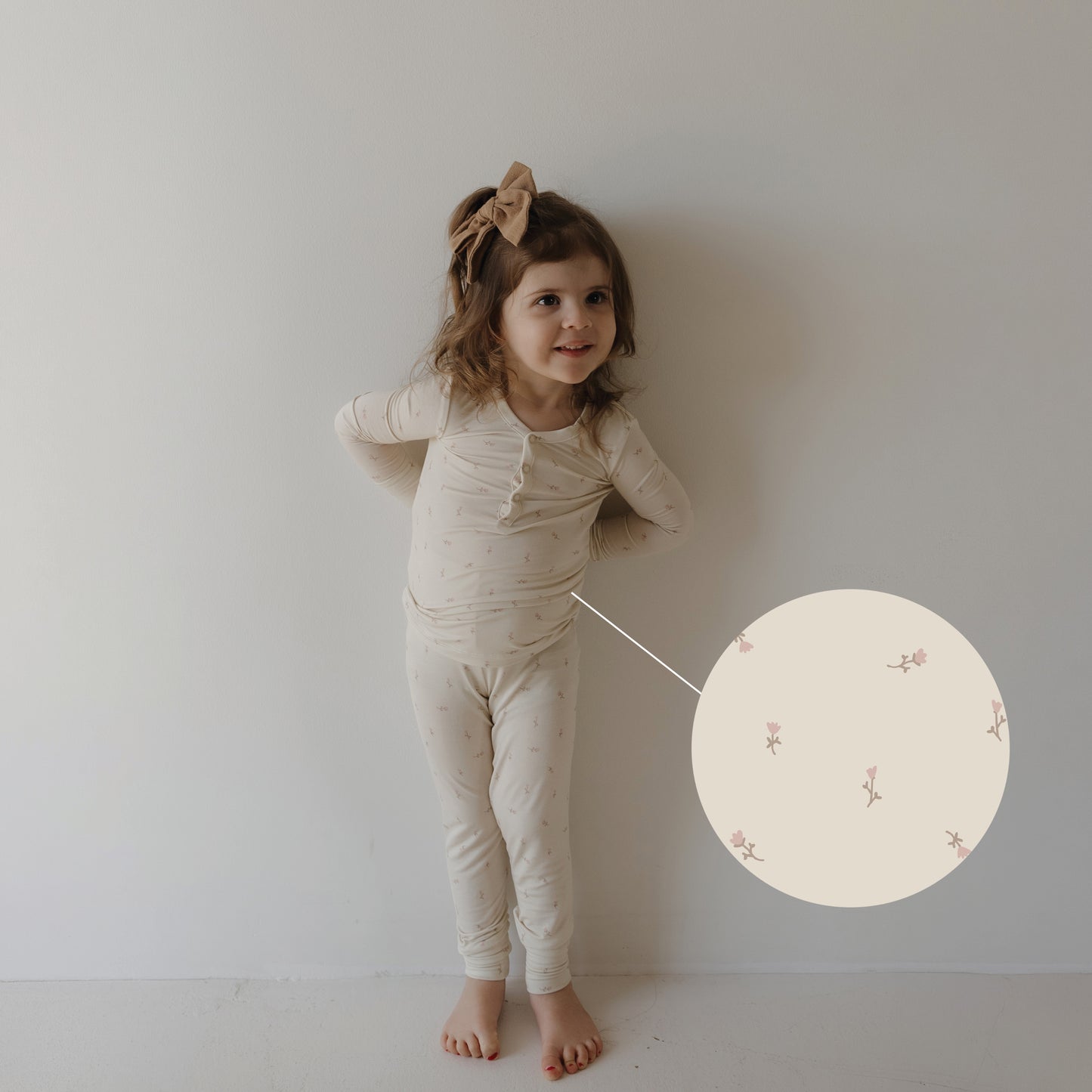 A young girl wears forever french baby’s Bamboo Two Piece Pajamas | Lucy, featuring a subtle pink floral print on cream. An enlarged circle highlights the soft, hypo-allergenic fabric designed for kids’ comfort.