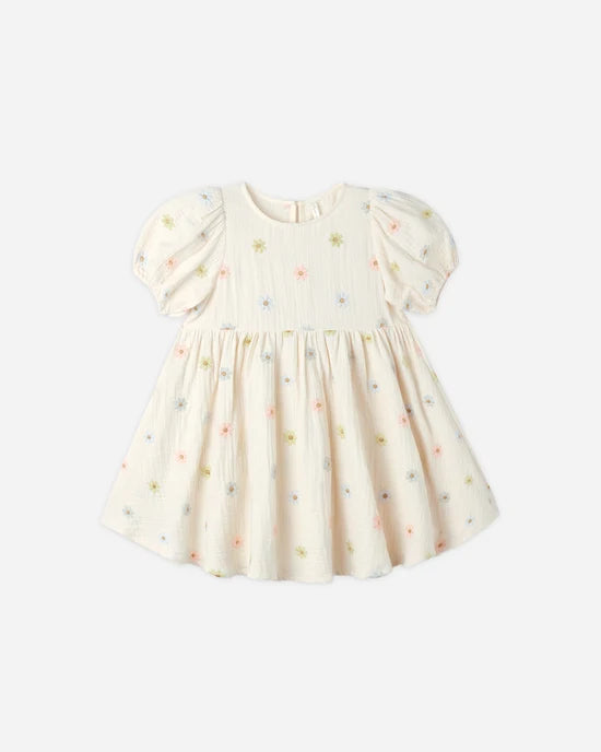 The Marley Dress by Rylee + Cru features a cream hue, short puff sleeves, a gathered waist, and delicate pastel embroidered daisies scattered across the fabric. It is shown against a plain light background.