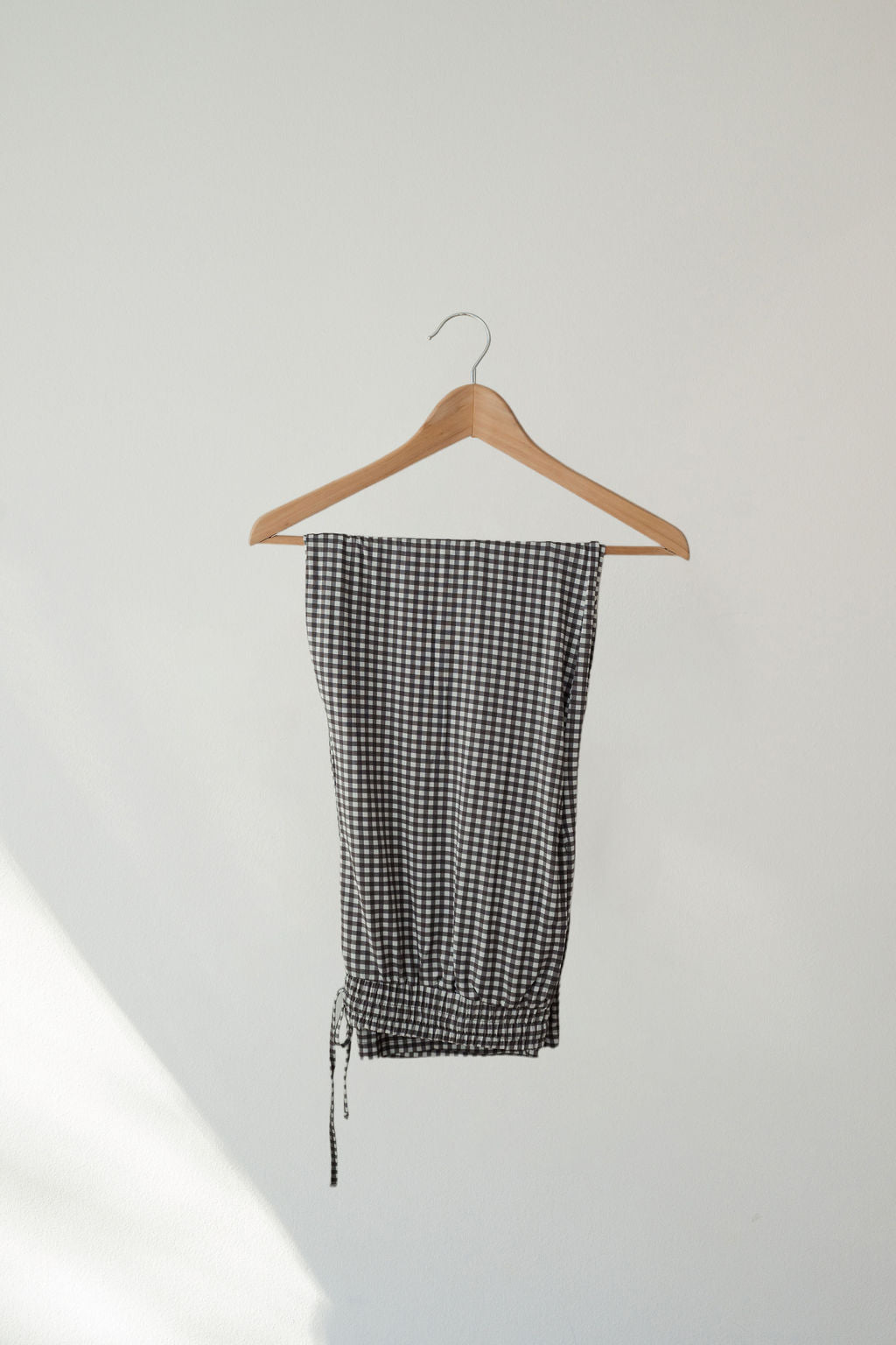 A pair of Men's Short Sleeve Pajamas in green gingham by forever french baby hangs neatly on a wooden hanger against a plain white wall.