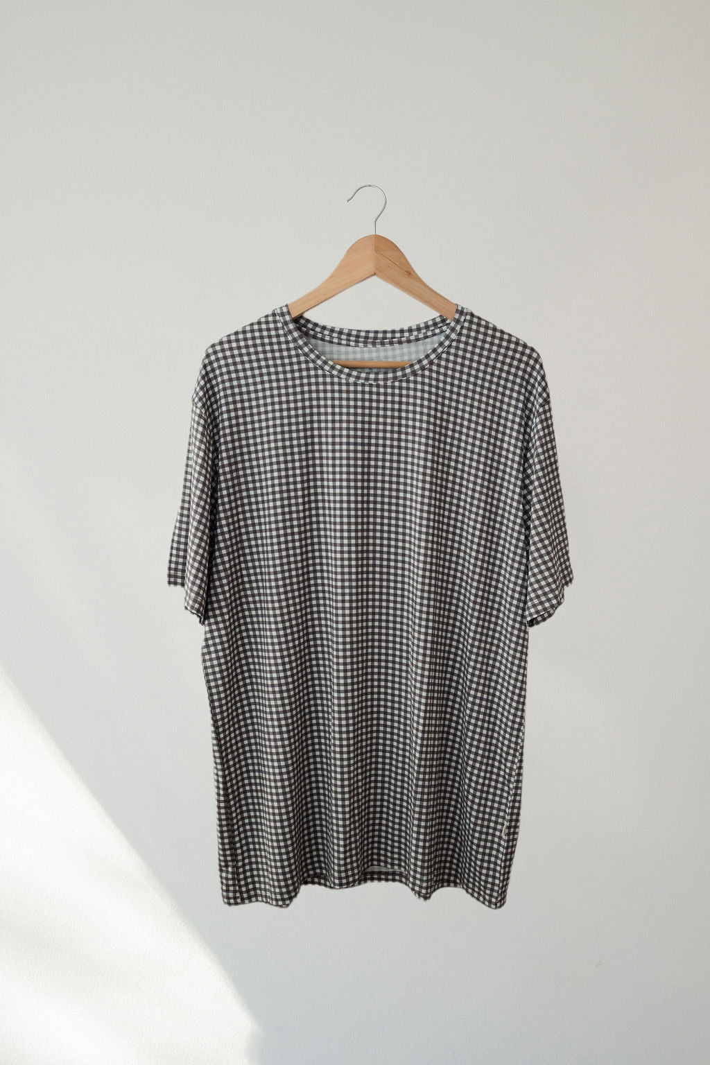 The Men's Short Sleeve Pajamas in Green Gingham by forever french baby, inspired by bamboo sleepwear, hang on a wooden hanger against a plain, light-colored wall.