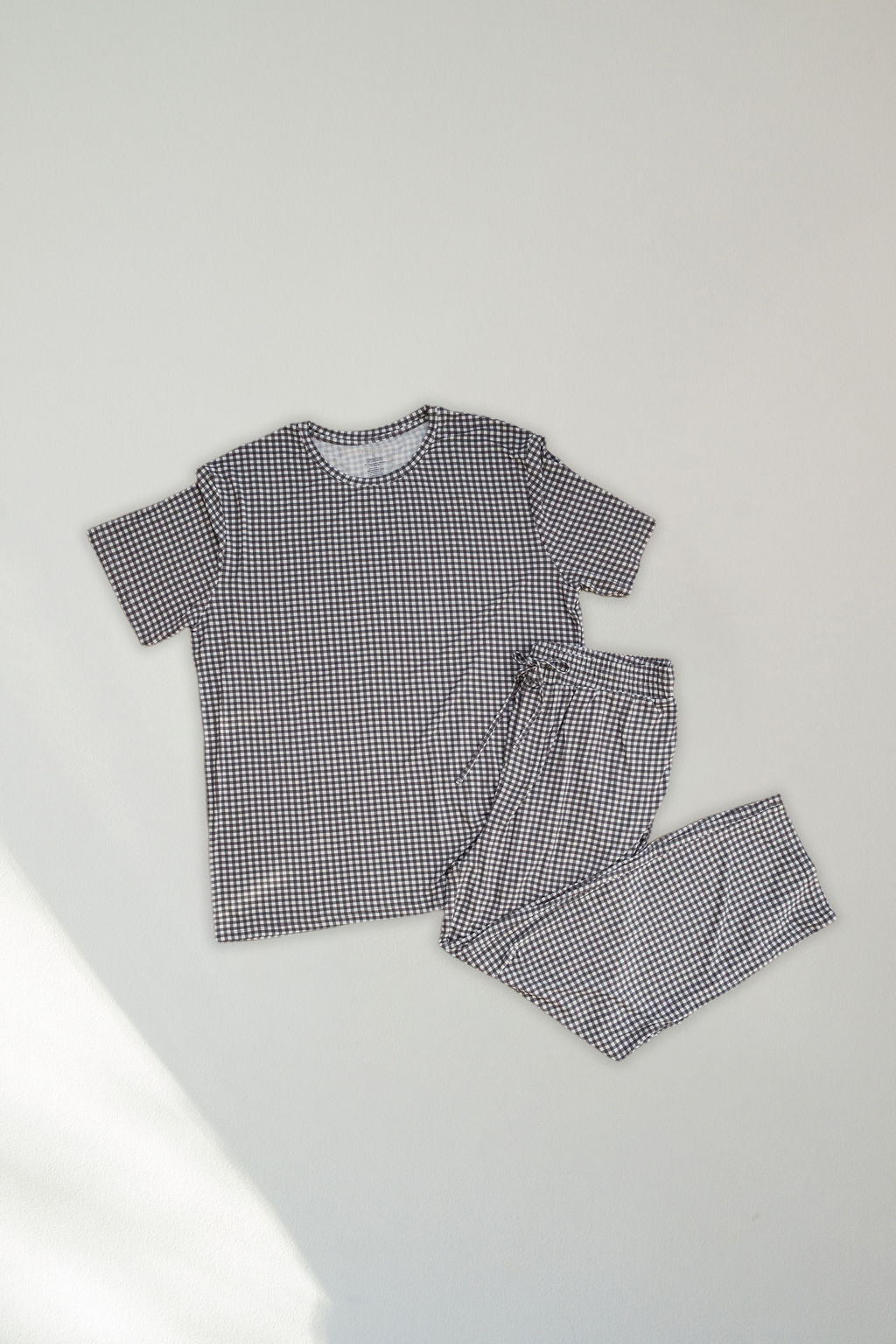 The Men's Short Sleeve Pajamas in Green Gingham by forever french baby, featuring a matching top and pants, are laid flat on a plain surface for stylish, hypoallergenic comfort.