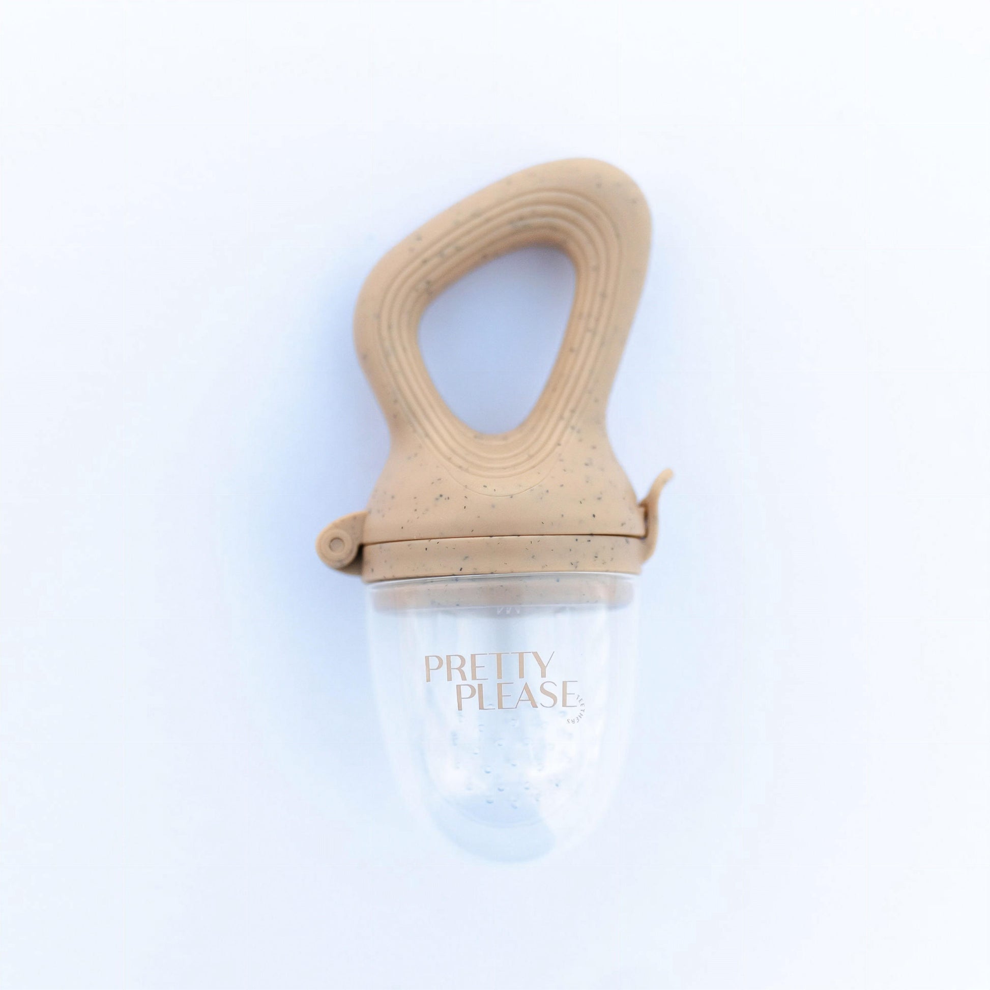 A beige, oval-shaped Modern Mod Feeder baby pacifier from forever french baby, featuring a speckled pattern and a clear silicone nipple, positioned on a white background. The words "PRETTY PLEASE" are printed in gold on the clear tip.