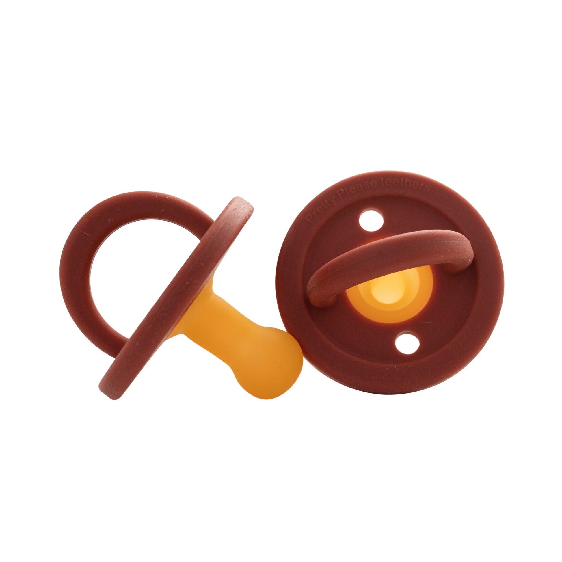 Two Modern Pacifier | Red Rock silicone pacifiers by forever french baby with brown circular shields and yellow nipples are shown. One pacifier is positioned upright with the ring handle visible, while the other lies flat, displaying its back—a perfect addition to your baby essentials collection.