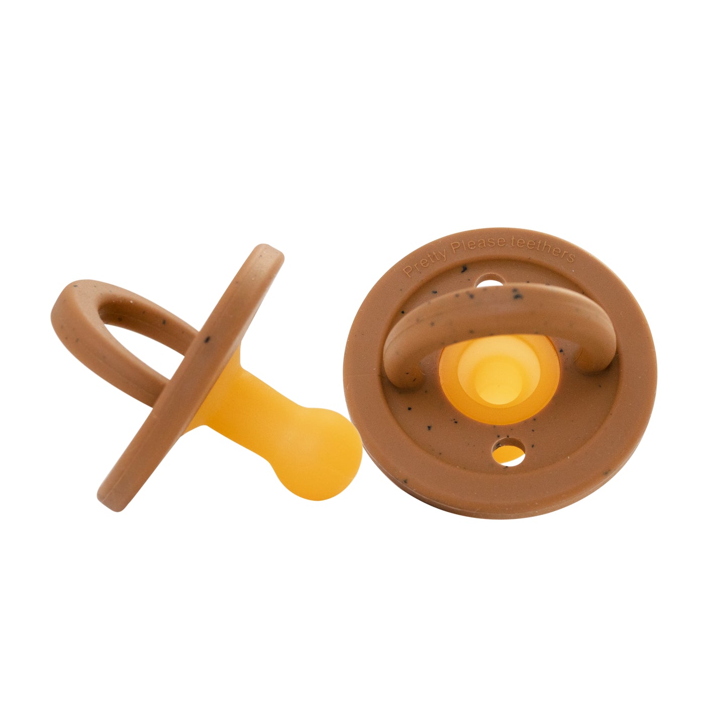 The set includes two Modern Pacifiers in the Speckled Almond design by forever french baby. One pacifier is laid flat, showcasing its ringed underside, while the other stands upright. Each silicone pacifier features a brown base speckled with almond patterns and a yellow nipple, seamlessly blending practicality with style.