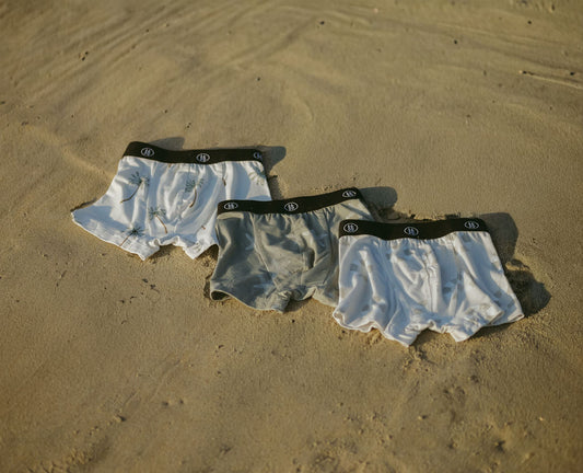 Three pairs of forever french baby Bamboo Boxers (3 Pack)—Lifesaver, Starfish & Palm Tree—featuring black waistbands are laid out on sand, offering ultra-soft bamboo comfort for kids with sensitive skin.
