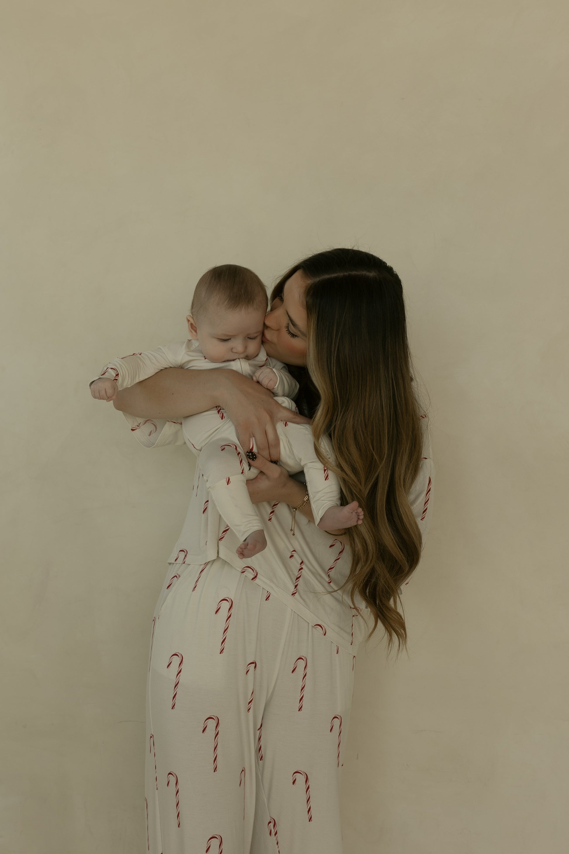 A woman with long brown hair kisses a baby while holding them, both dressed in forever french baby's matching Women's Boxy Tee Lounge Set | Candy Cane against a neutral background.
