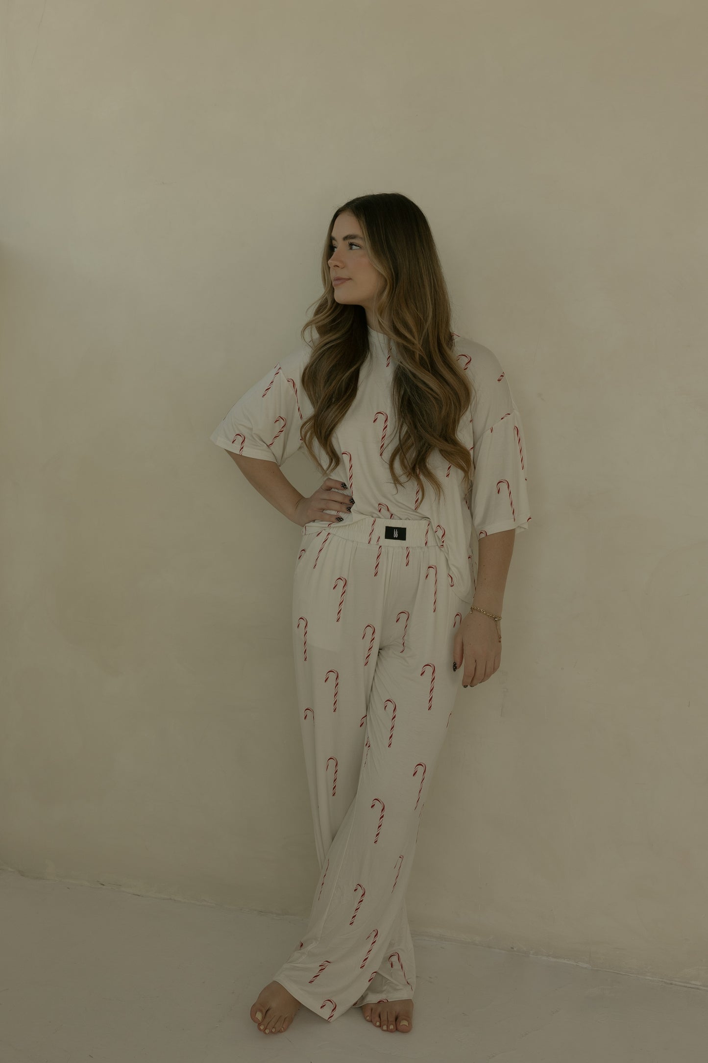 A woman with long hair stands barefoot against a beige wall, wearing the forever french baby Women's Boxy Tee Lounge Set in Candy Cane—an ultra-soft, hypoallergenic bamboo outfit perfect for lounging or sleep. She has one hand on her hip and looks to the side.